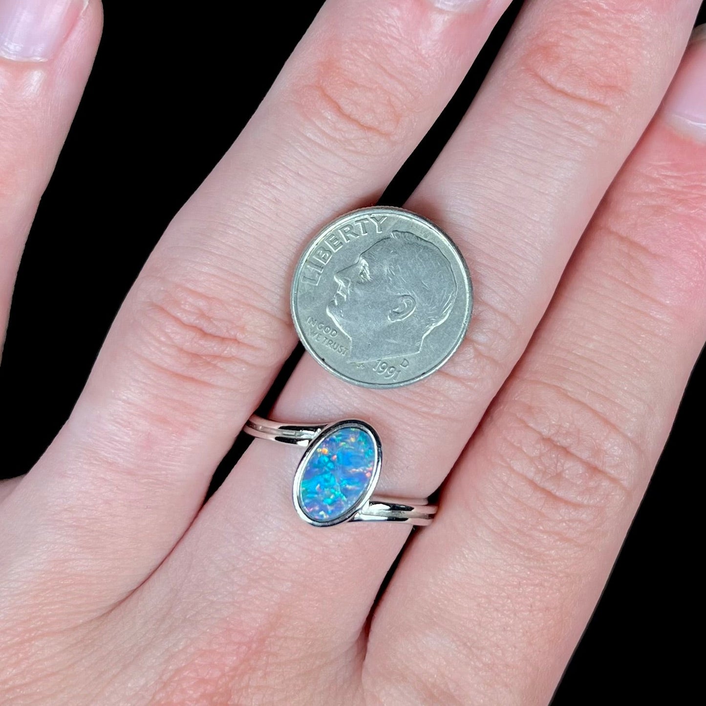 A sterling silver ring bezel-set with an oval shaped black opal doublet. The opal has red and blue fire.