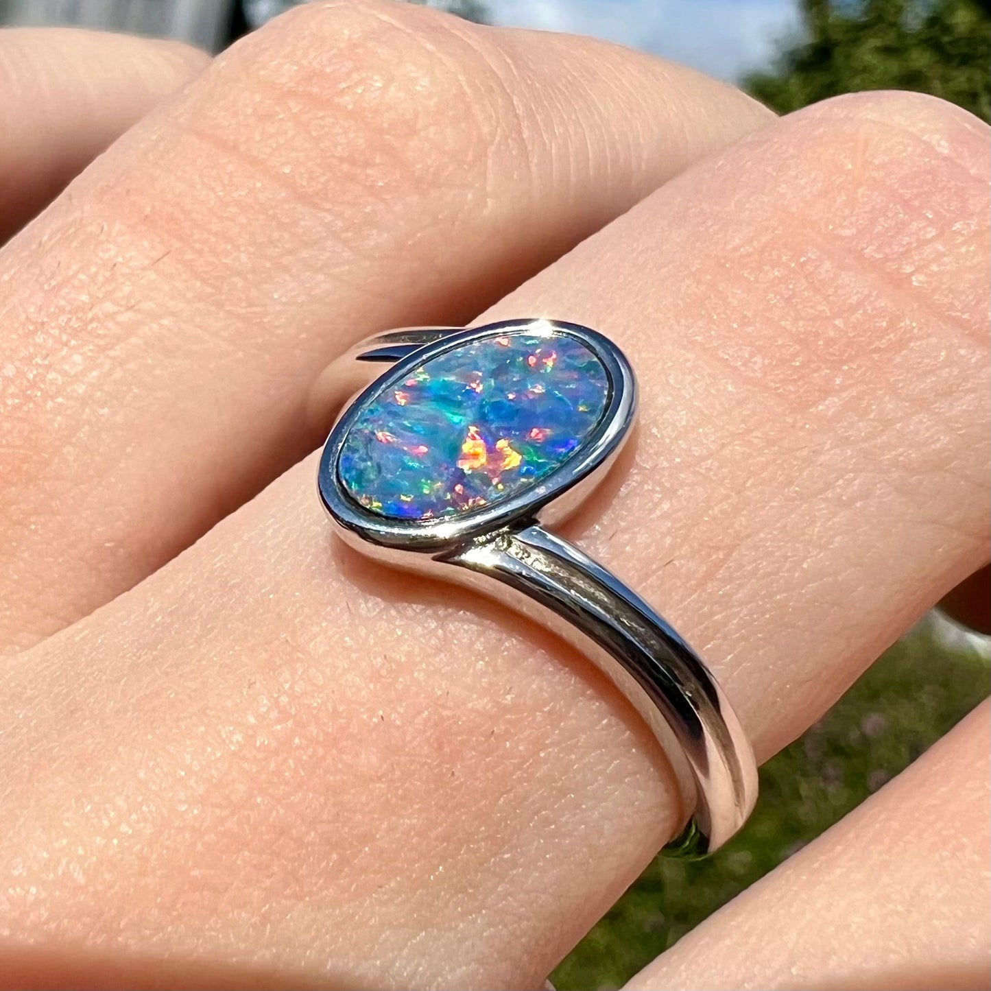 A sterling silver ring bezel-set with an oval shaped black opal doublet. The opal has red and blue fire.