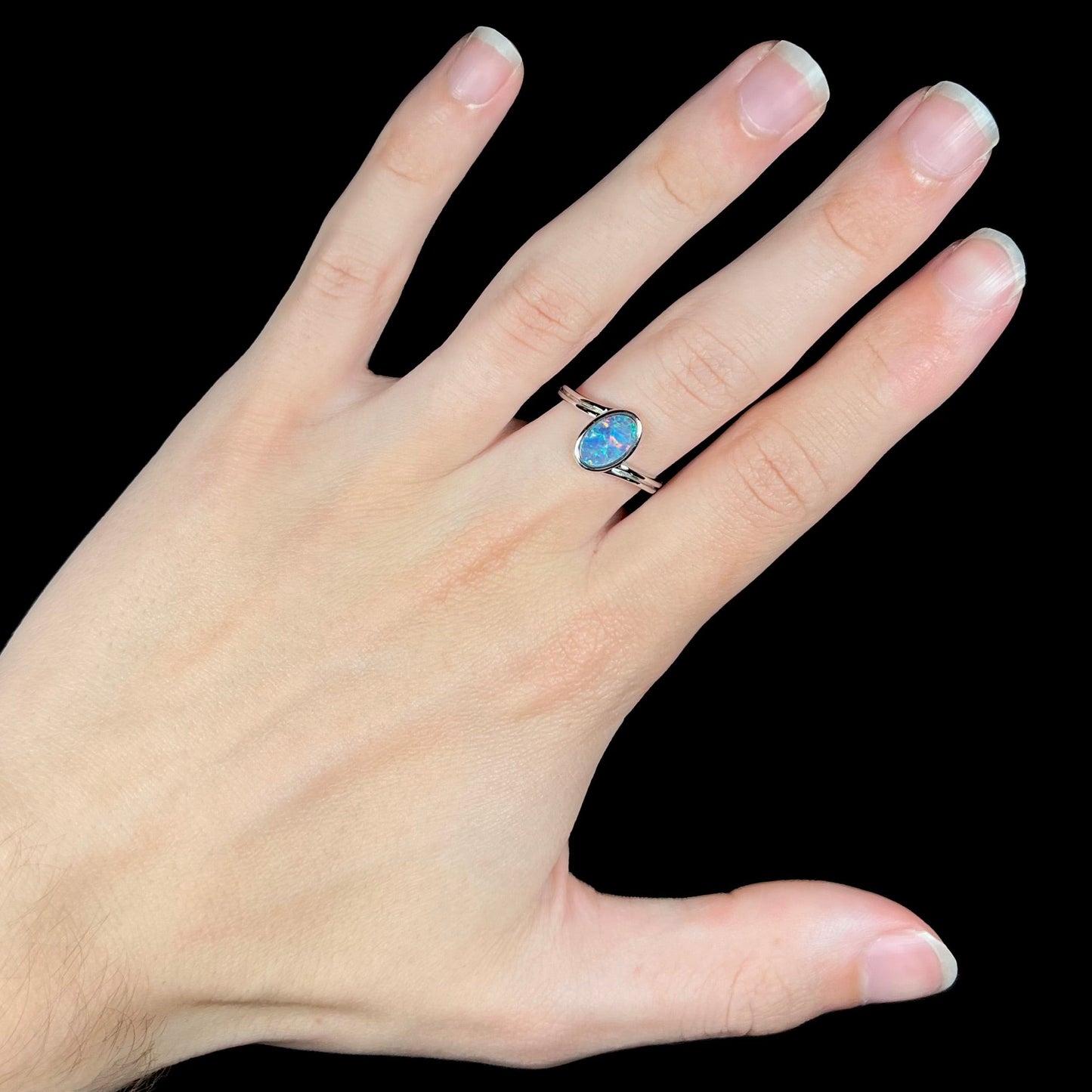 A sterling silver ring bezel-set with an oval shaped black opal doublet. The opal has red and blue fire.