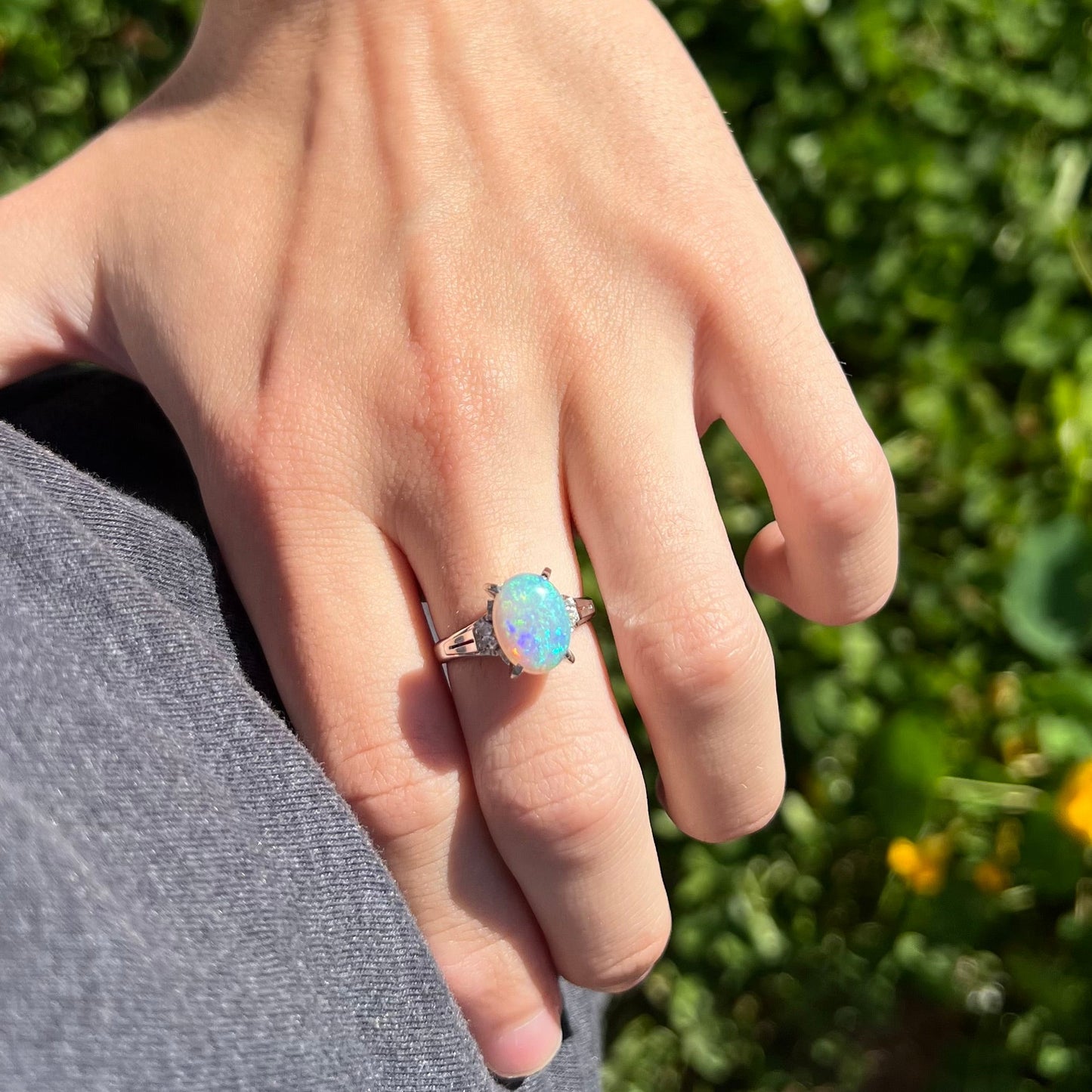 A platinum filigree opal engagement ring set with diamond accents. The opal has green-blue colors.