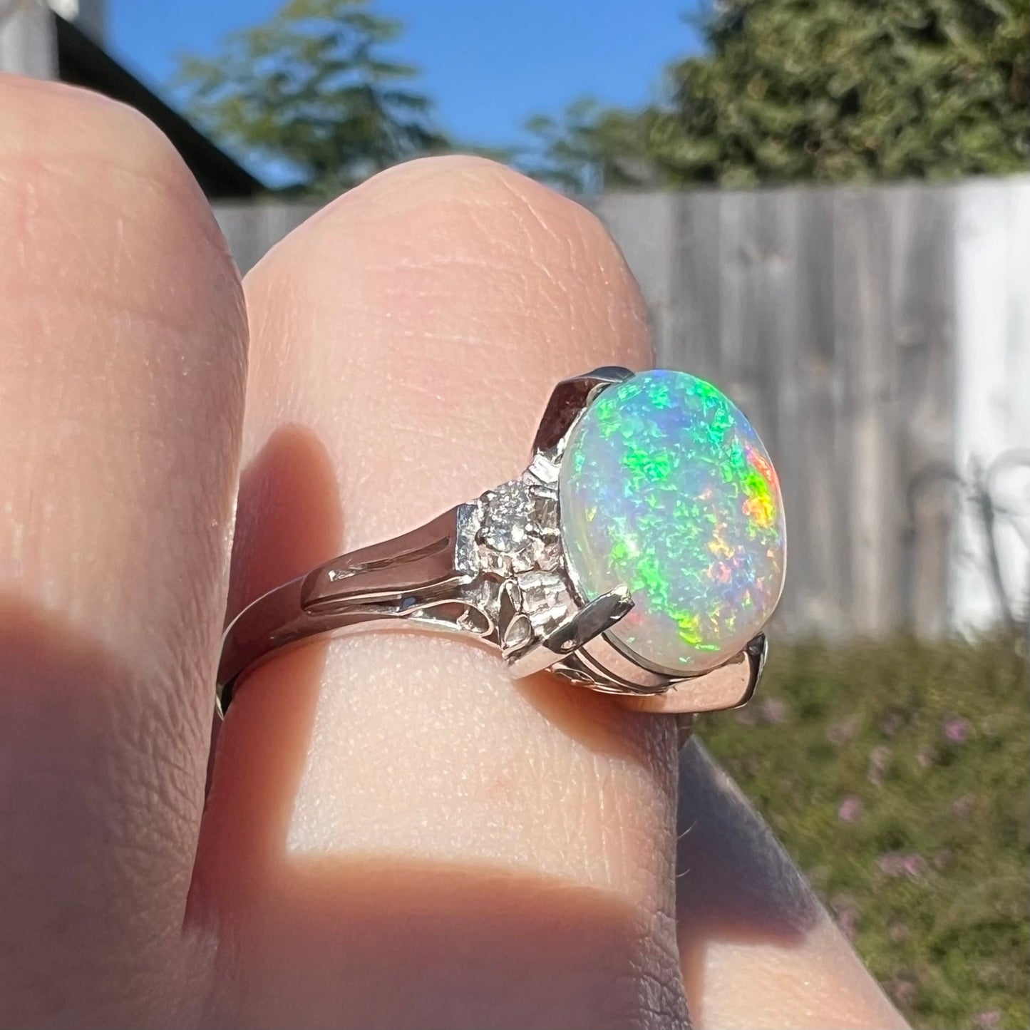 A platinum filigree opal engagement ring set with diamond accents. The opal has green-blue colors.