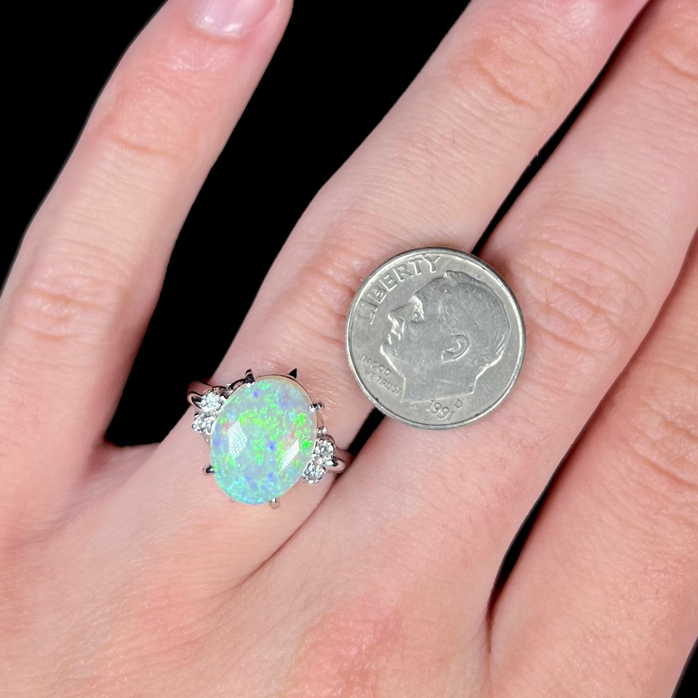 An Australian crystal opal and diamond engagement ring set in a platinum filigree mounting. The opal plays green/blue colors and has a crack.