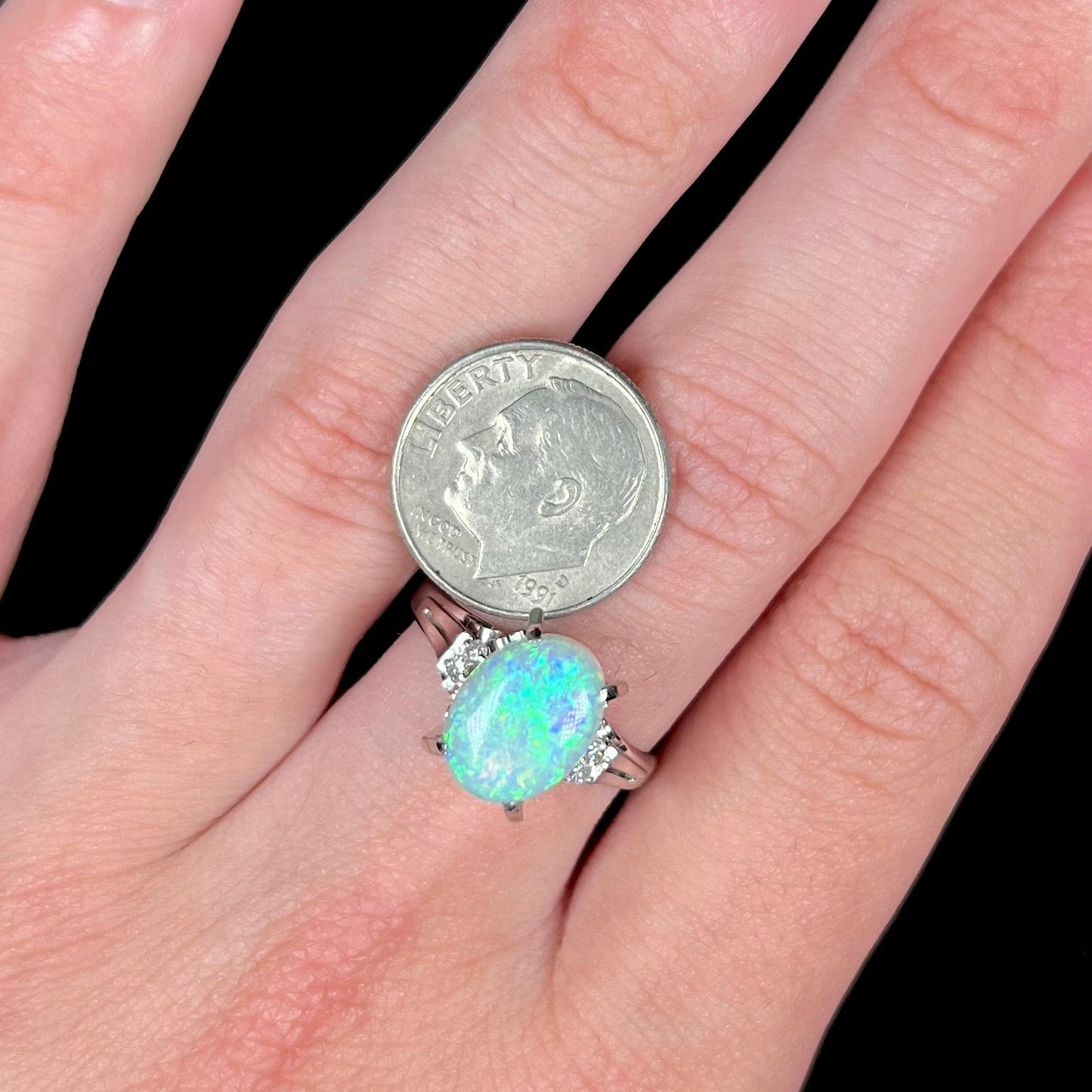 A platinum filigree opal engagement ring set with diamond accents. The opal has green-blue colors.