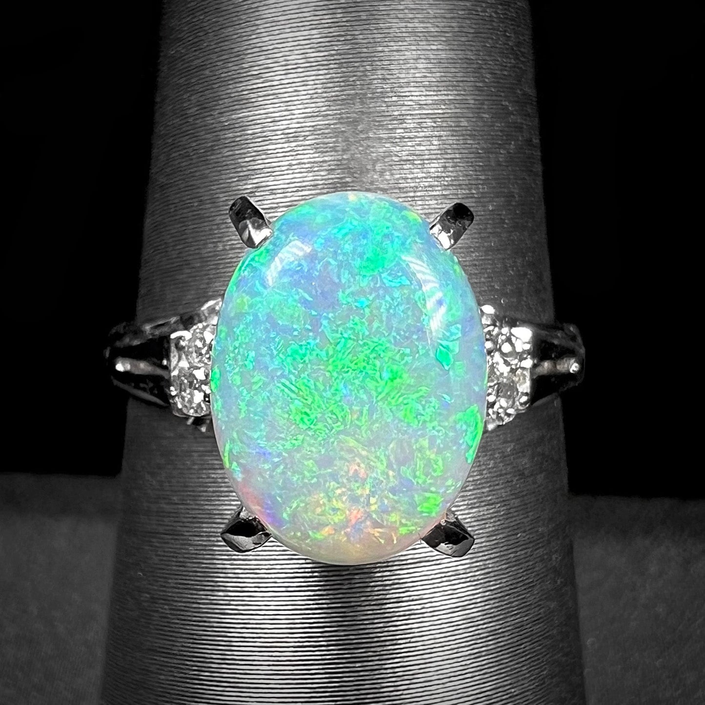 A platinum filigree opal engagement ring set with diamond accents. The opal has green-blue colors.
