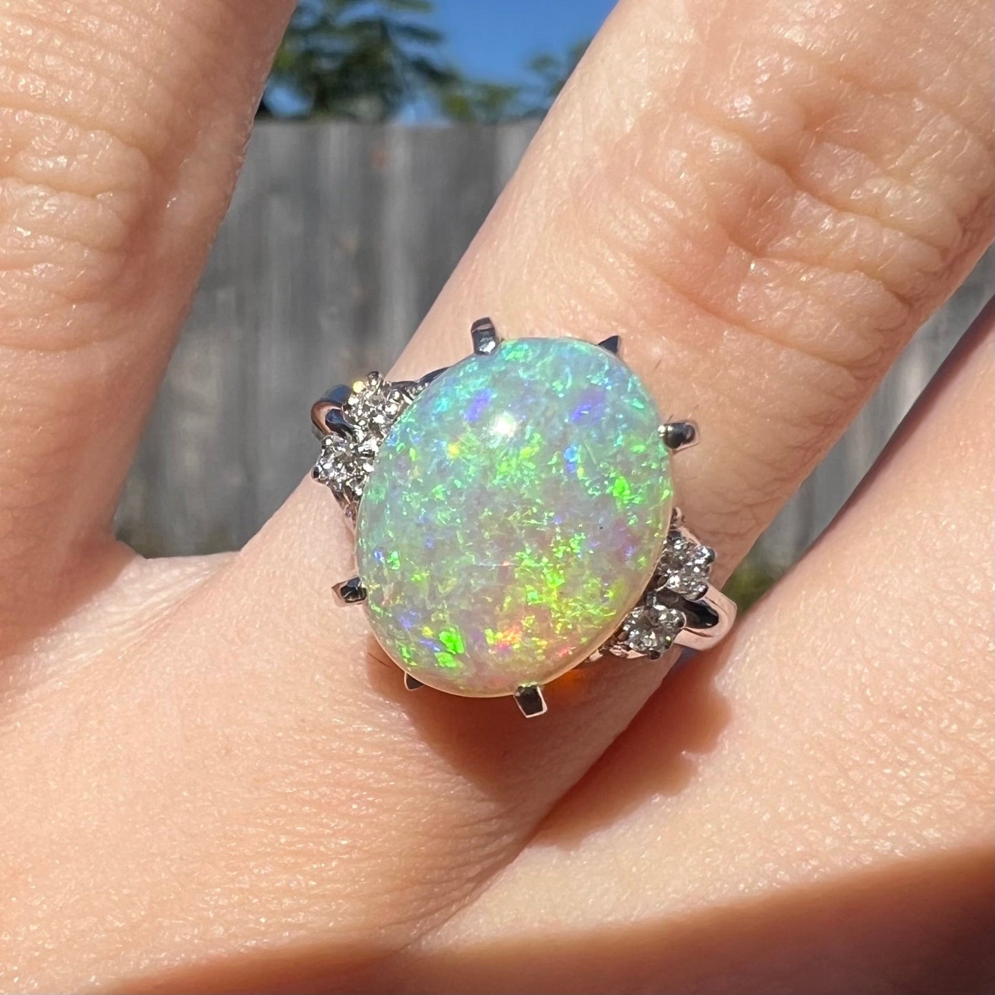 An Australian crystal opal engagement ring set with diamonds in a platinum filigree mounting. The opal plays green/blue colors and has a crack.