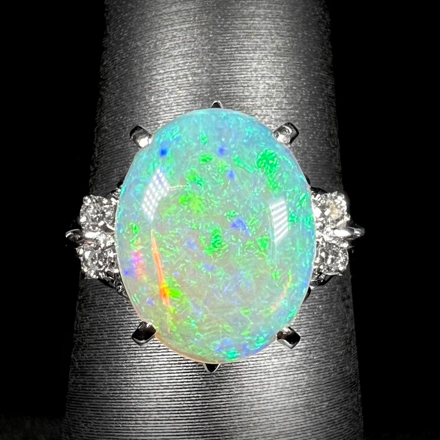 An Australian crystal opal and diamond engagement ring set in a platinum filigree mounting. The opal plays green/blue colors and has a crack.