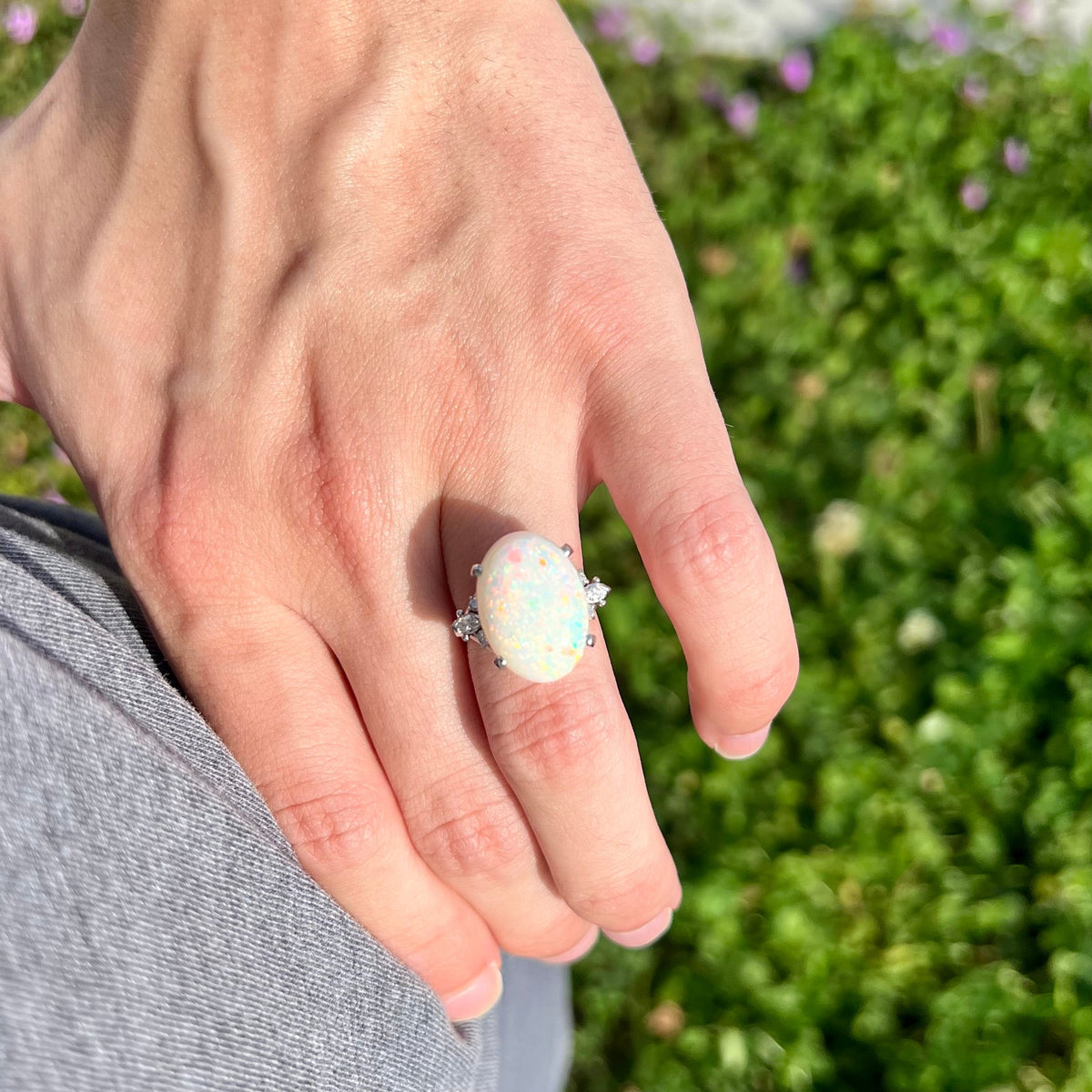Close-up of person's hand resting on hip in sunlight wearing a 7.97ct Australian white opal and diamond cocktail ring.