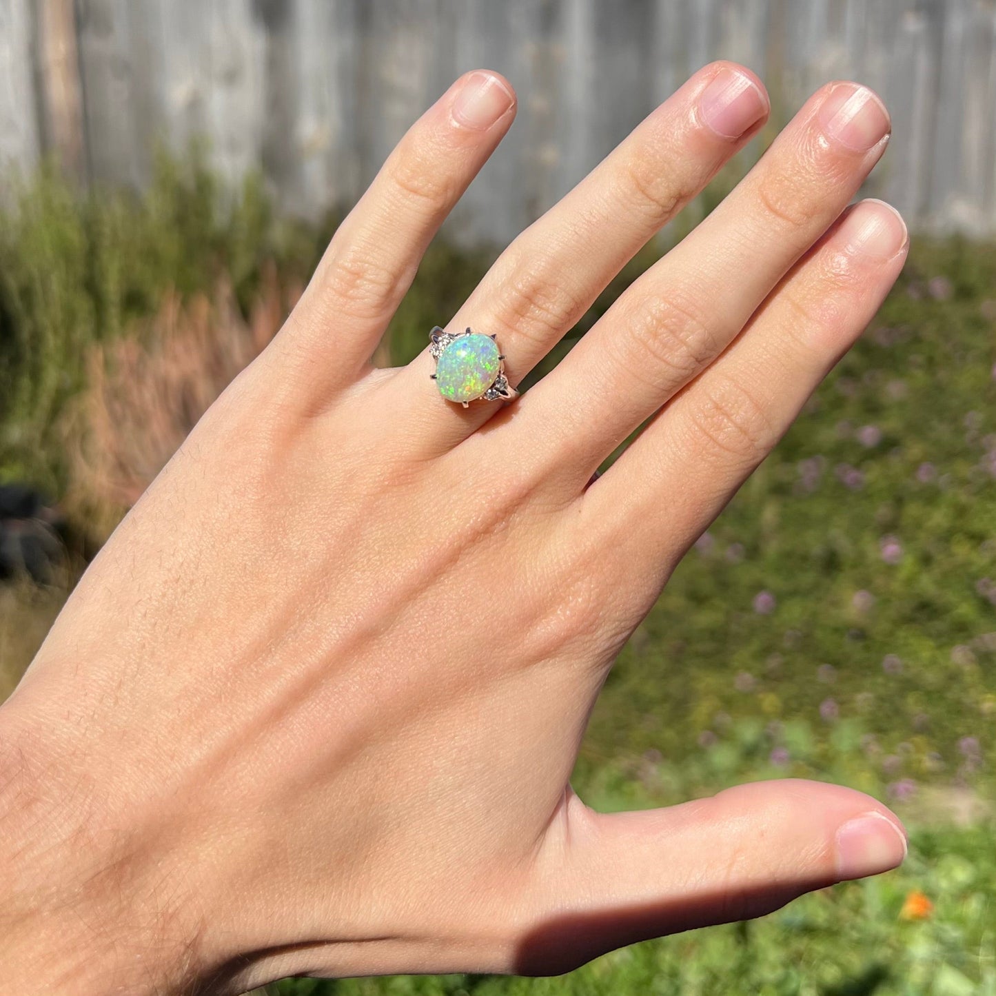 An Australian crystal opal and diamond engagement ring set in a platinum filigree mounting. The opal plays green/blue colors and has a crack.