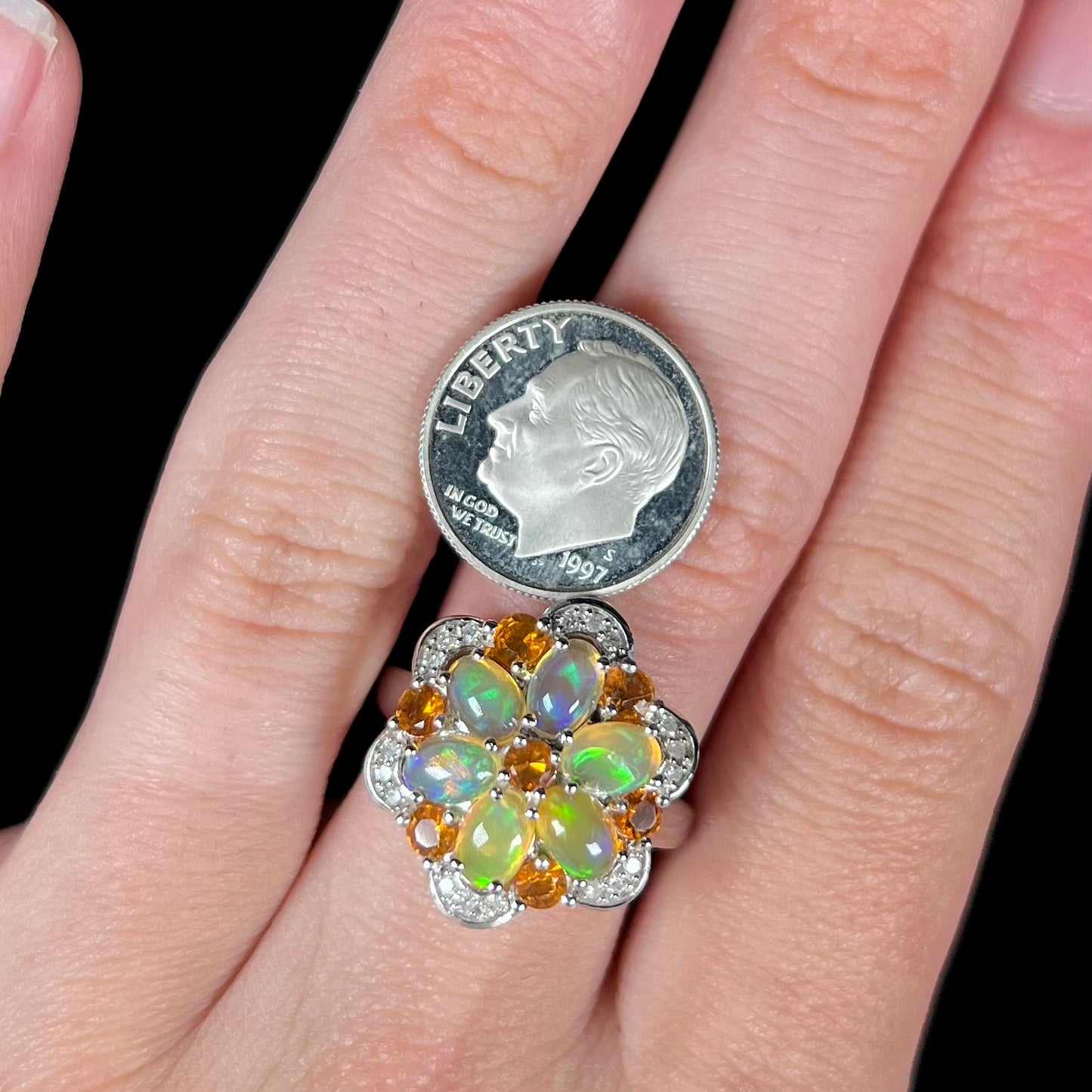An opal flower-design cluster ring worn on a finger next to a dime coin for scale.