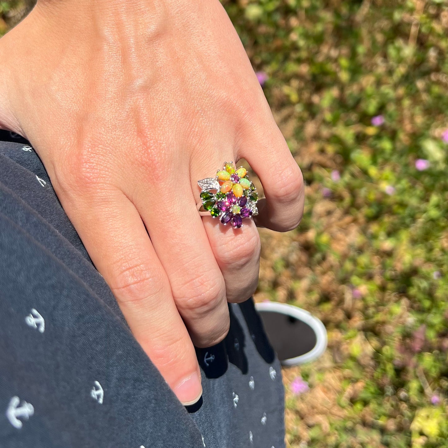 A multi-stone opal flower ring worn on a hand as it rests on the model's hip in an outdoor setting.
