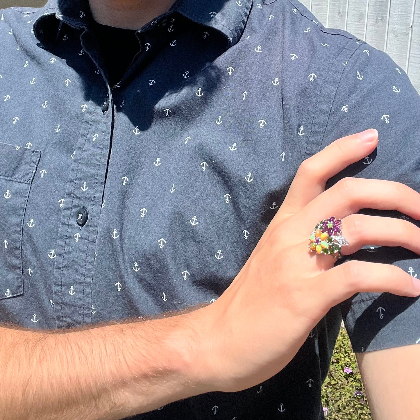 A multi-gemstone opal flower ring worn on a hand as it rests on the model's opposing shoulder.