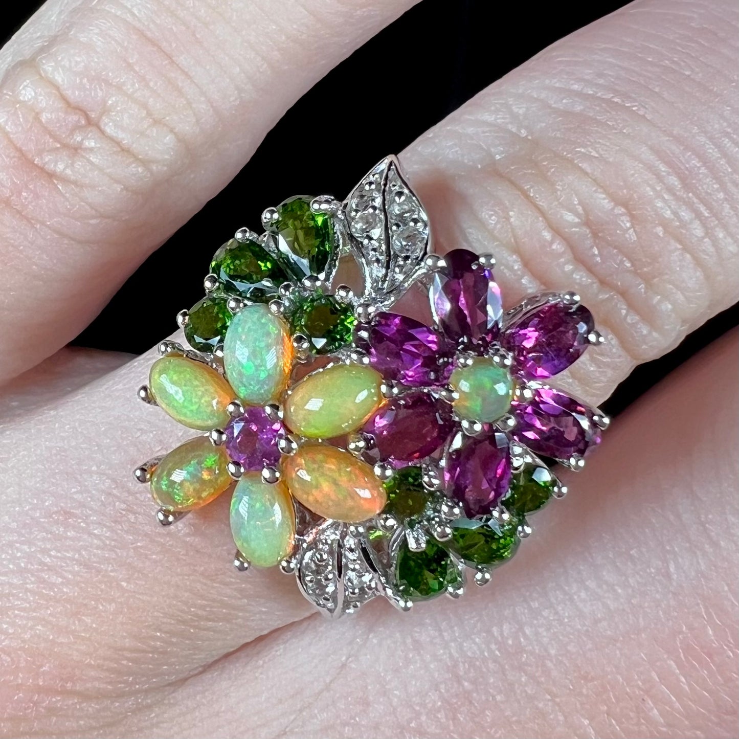 A fire opal, garnet, and chrome diopside flower ring shown close-up, worn on a finger.