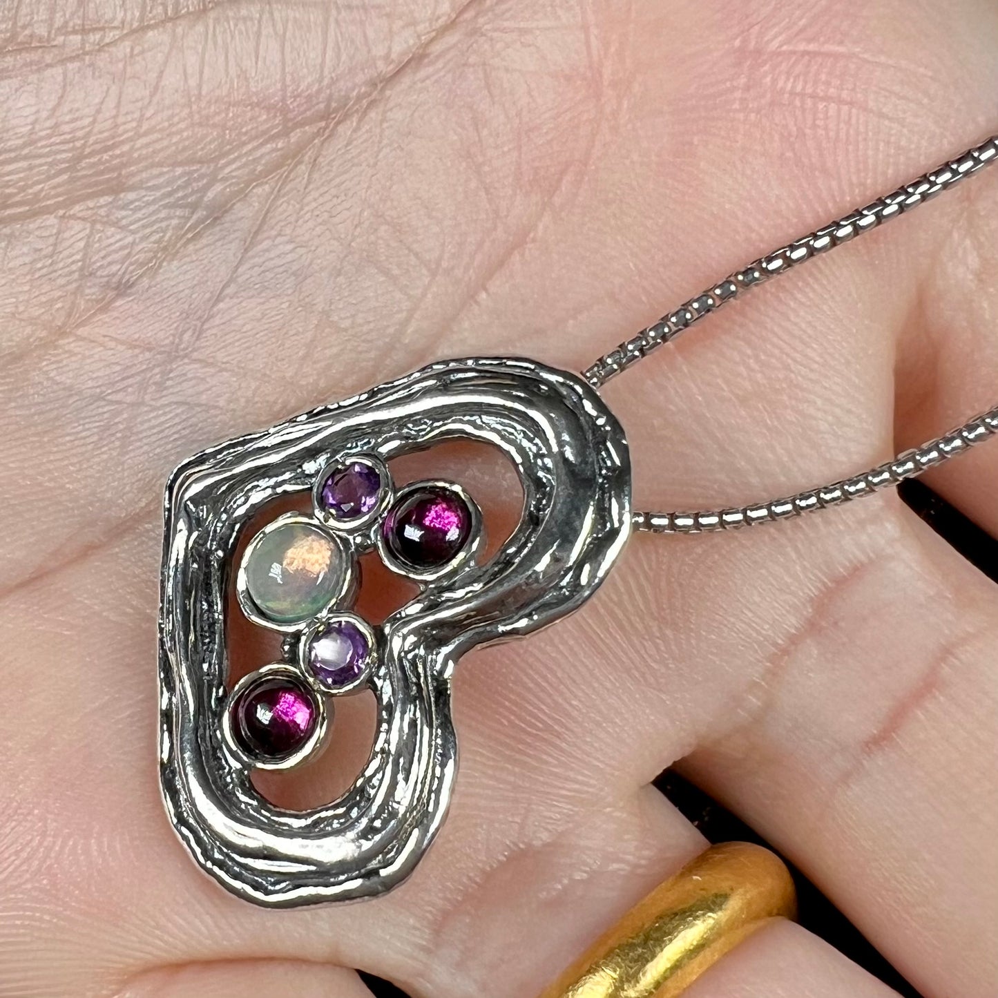 A sterling silver heart necklace set with a round Ethiopoian opal, two amethysts, and two rhodolite garnets.