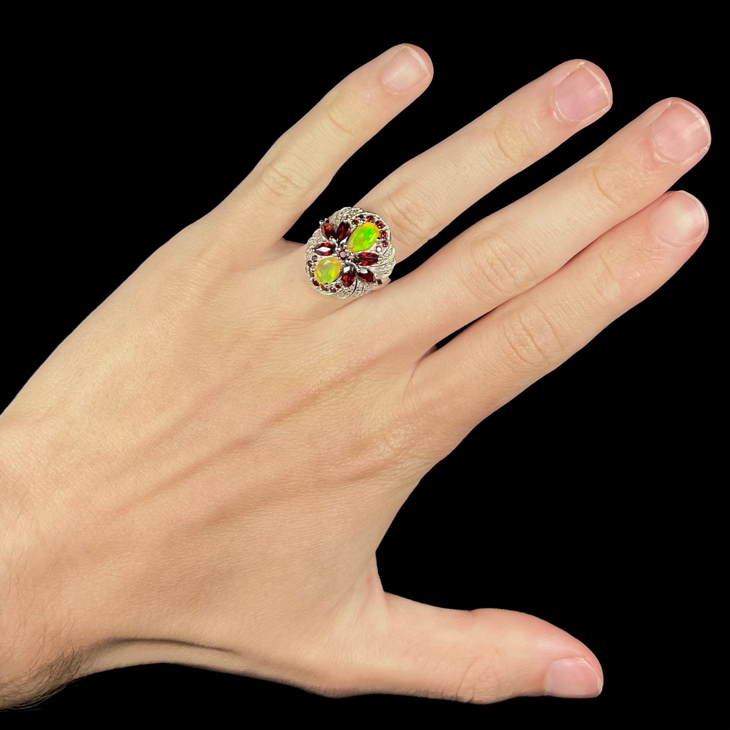An opal and garnet infinity-design ring, worn on a hand against a black background in LED light.