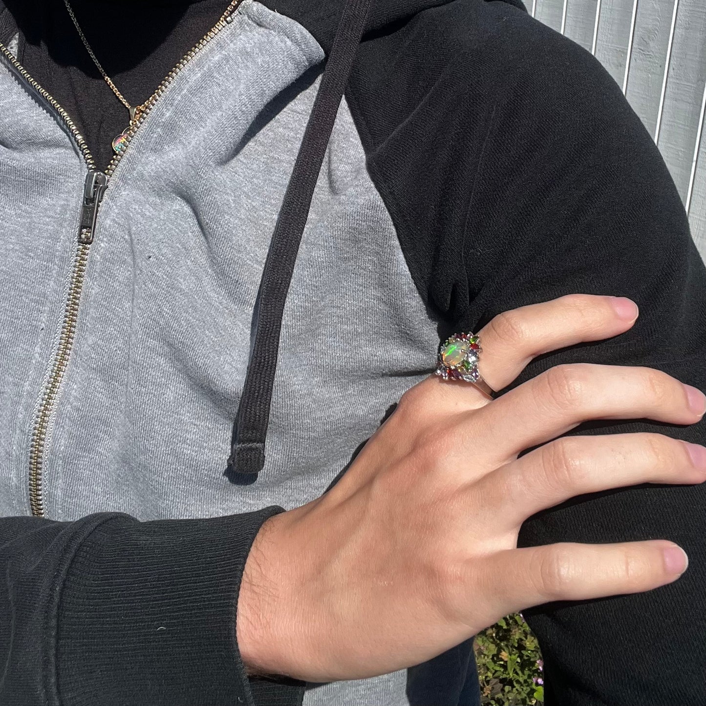 An opal and multi-color gemstone ring worn on a hand that's resting on the model's shoulder.