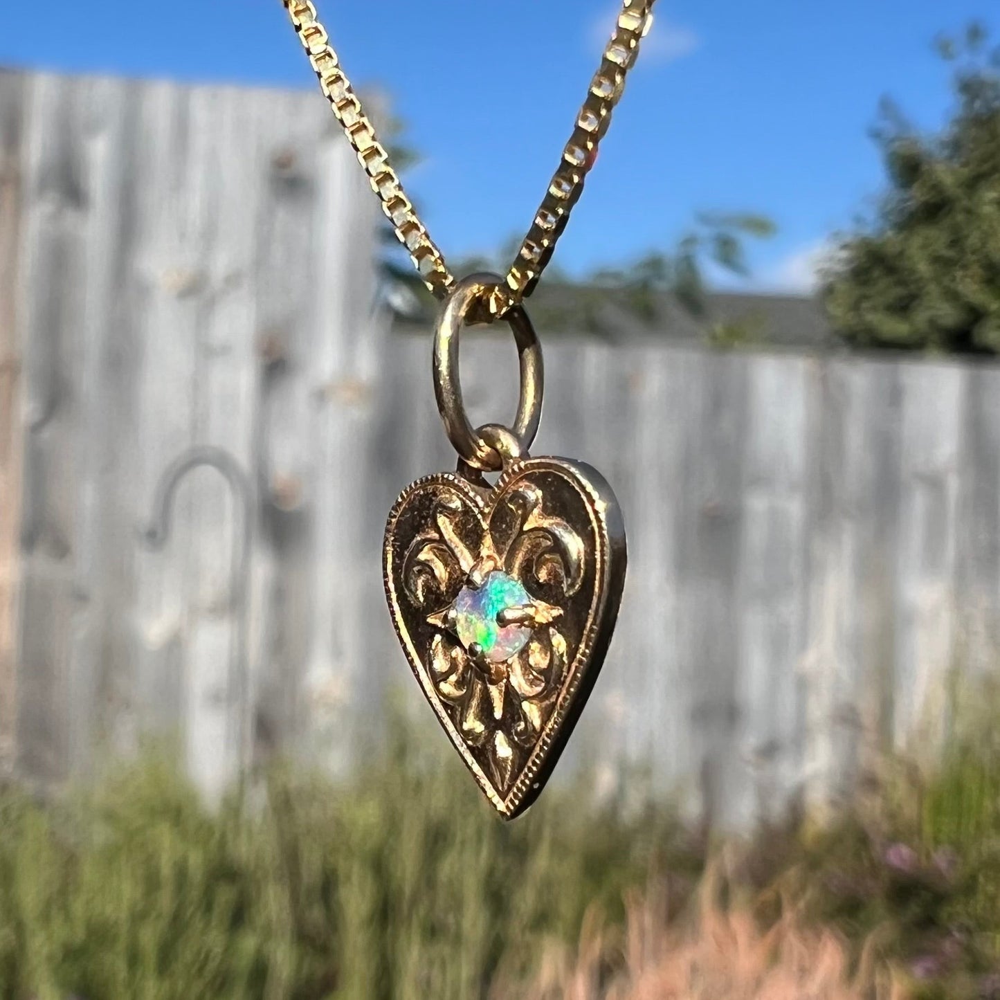 A yellow gold filigree heart necklace mounted with a round, green Australian crystal opal stone.