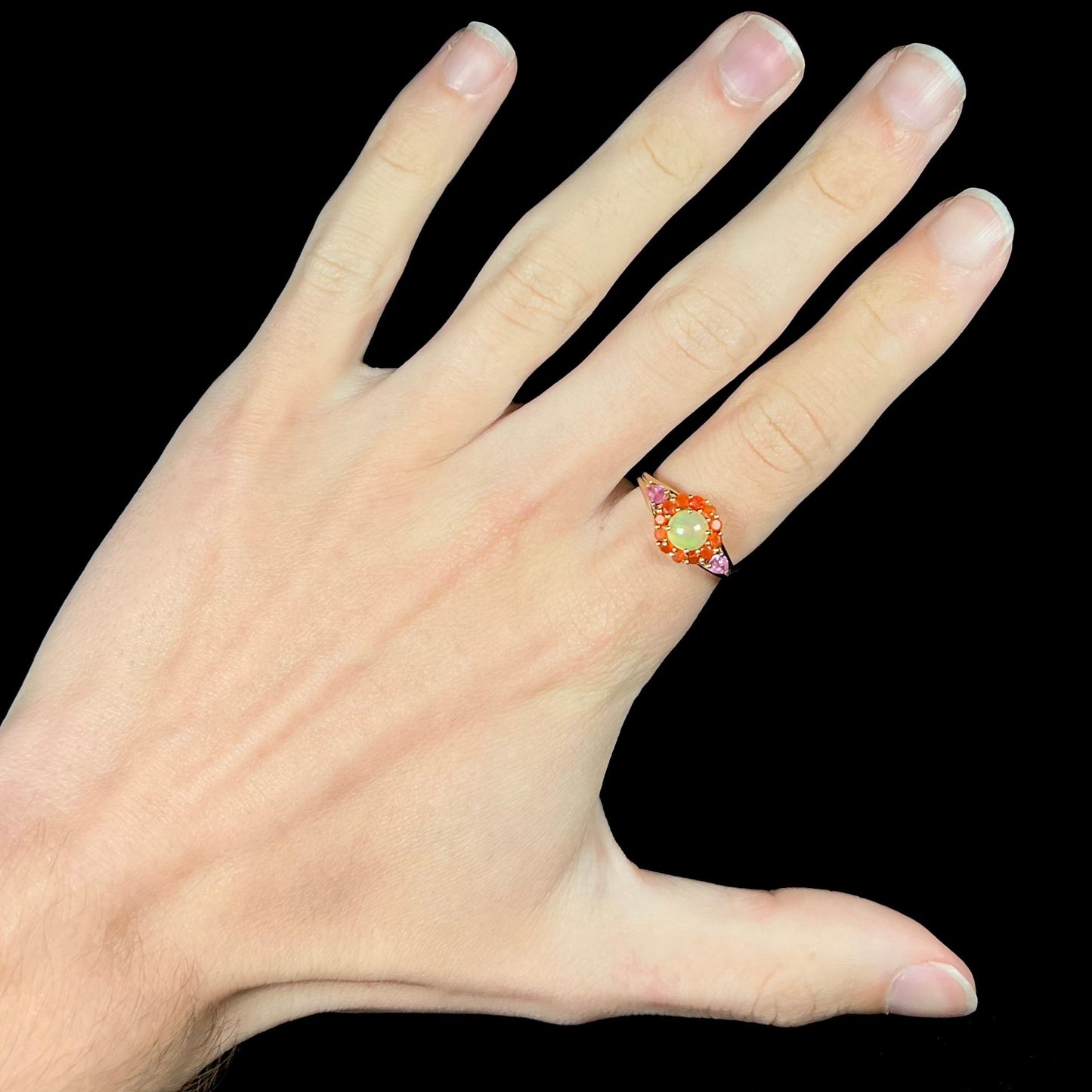 A yellow gold ring mounted with a round Ethiopian opal in a halo of faceted Mexican fire opals. Two pear shaped pink tourmalines accent the sides of the ring.