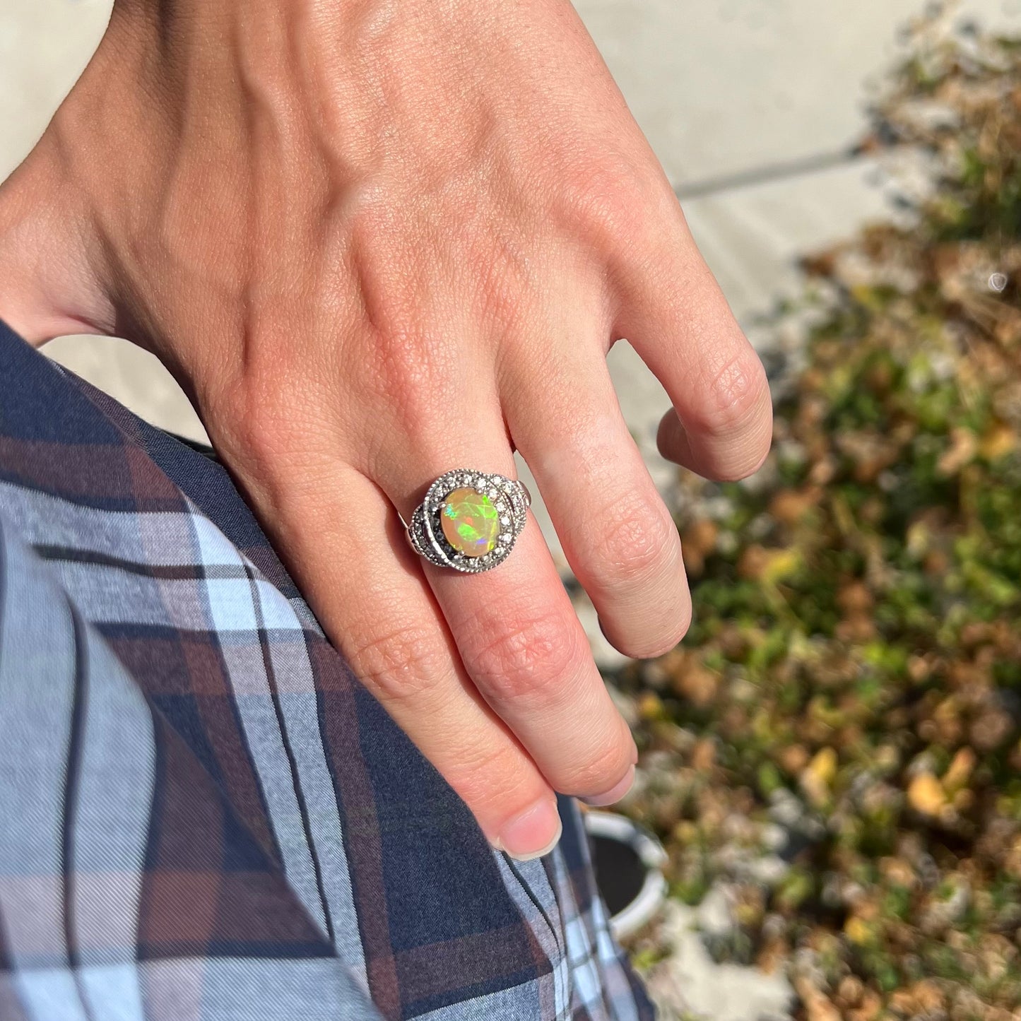 A hand resting on hip while wearing an Ethiopian opal halo ring with green color play in the sunlight.