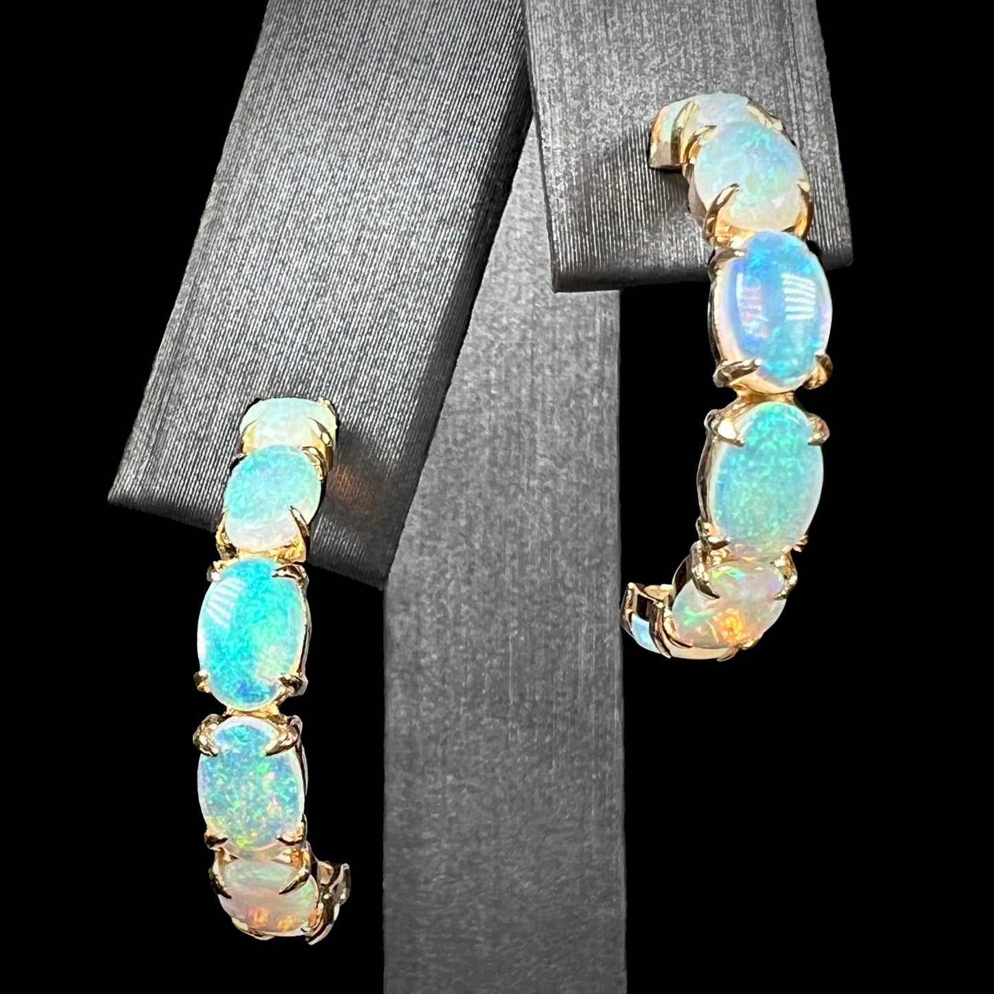 A pair of crystal opal hoop earrings in 14k gold on a black background, front macro view.