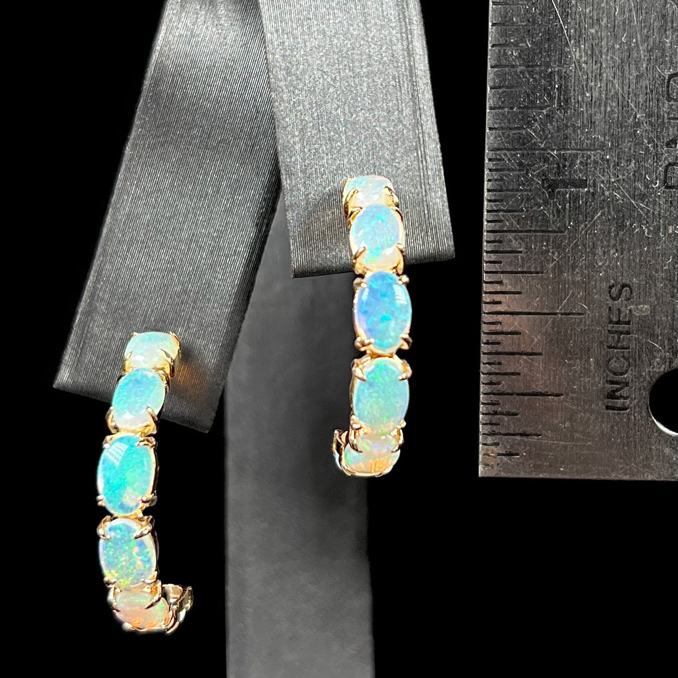 Gold opal hoop earrings next to a ruler for size reference, measuring just under one inch.
