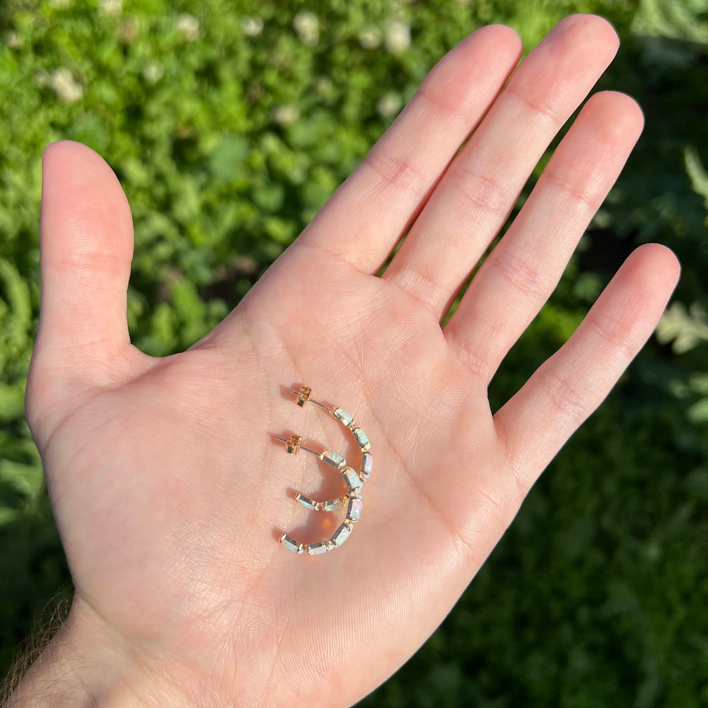 Crystal opal hoop earrings held in palm outdoors, showing curved semi-hoop design.