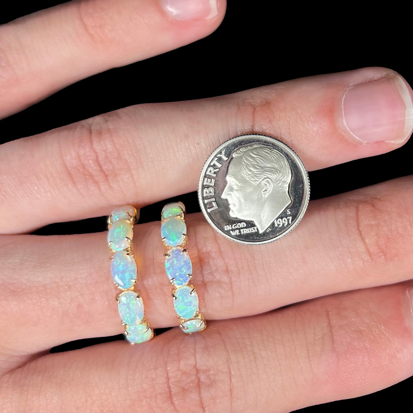 Crystal opal earrings wrapped around a finger, with a dime for scale.