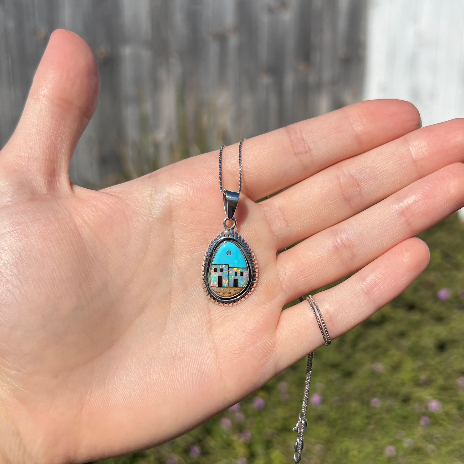 A Southwest-style silver opal and turquoise inlay necklace, shown in a hand in the sunlight.