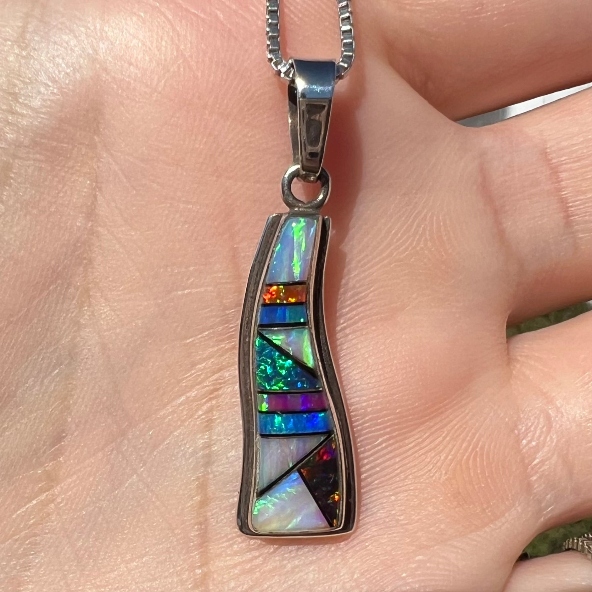 Close-up sunlit view of a silver Navajo opal inlay necklace, held in a hand.