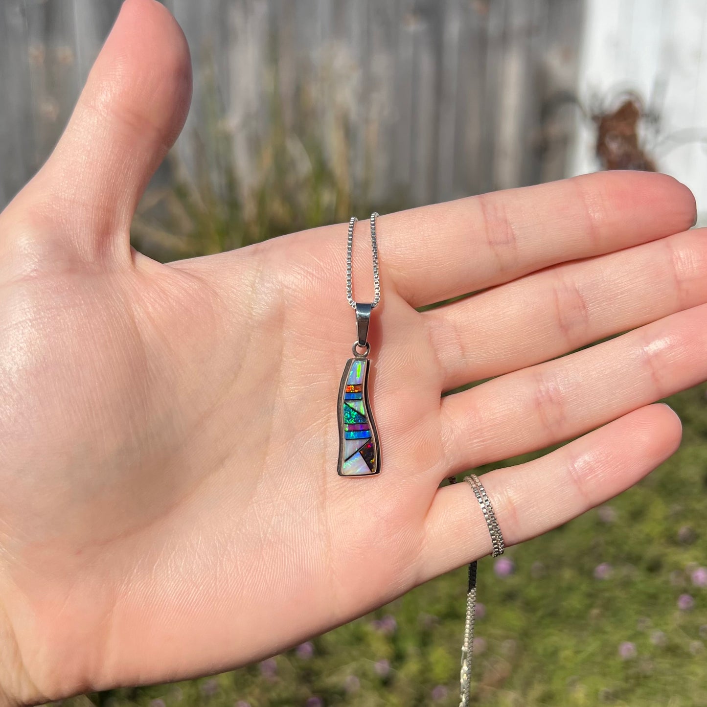 A sterling silver opal inlay necklace, held in a hand and shown from a distance in the sunlight.