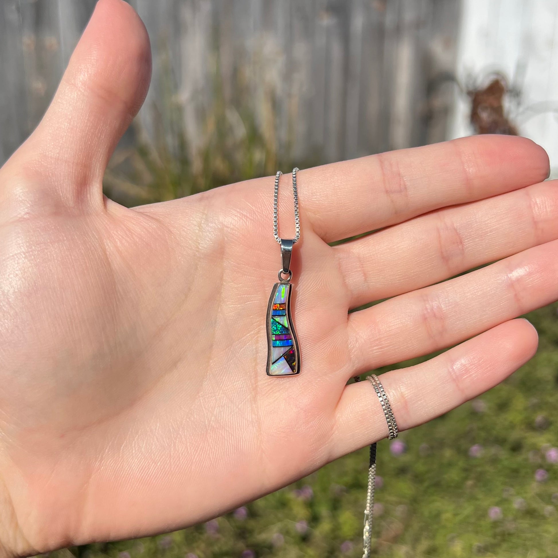 A sterling silver opal inlay necklace, held in a hand and shown from a distance in the sunlight.