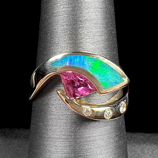 A 14k gold twisted shank ring set with a triangle cut pink tourmaline, green semi-black opal inlay, and three flush-set diamonds.
