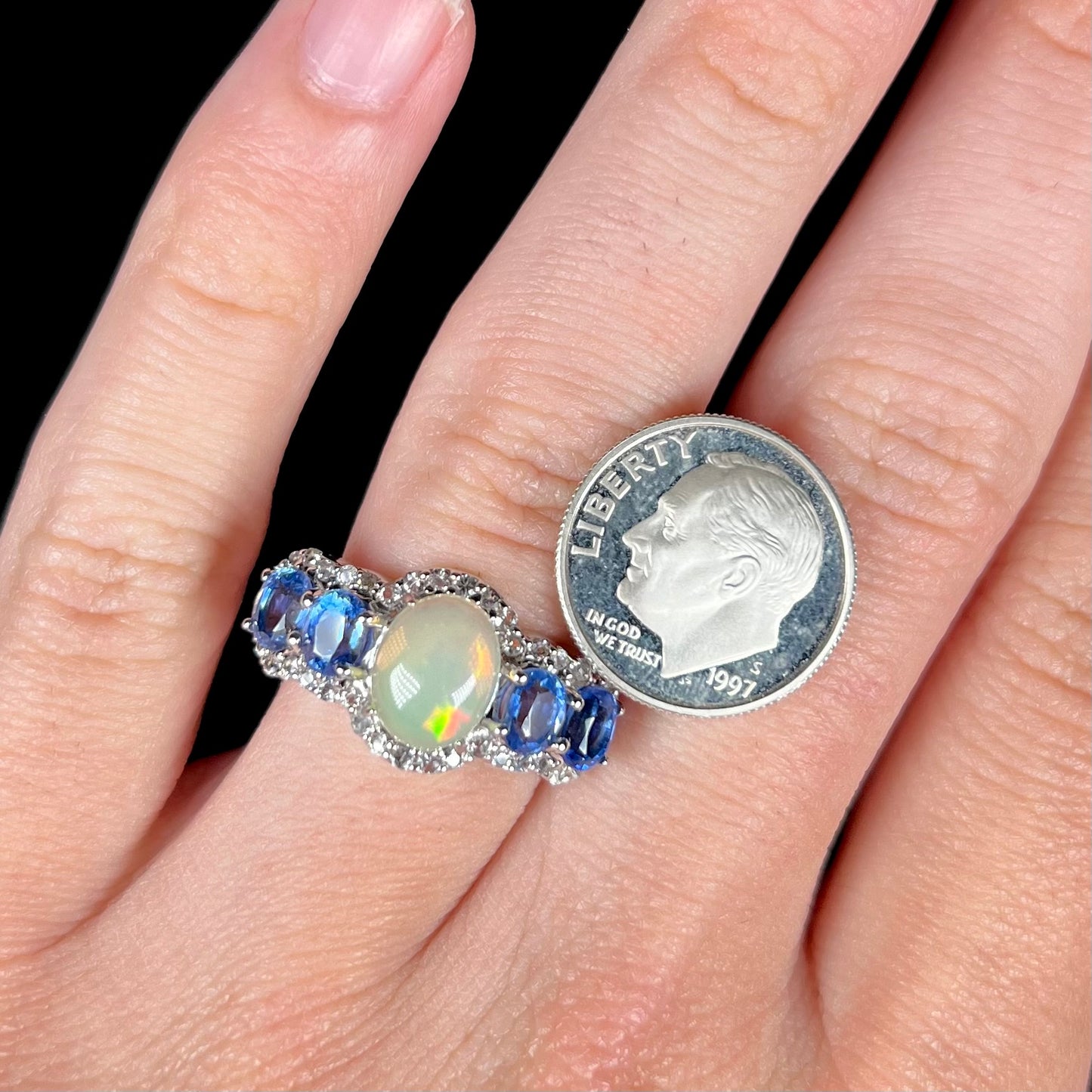Close-up of a sterling silver Ethiopian opal and kyanite ring worn on a hand next to dime coin.