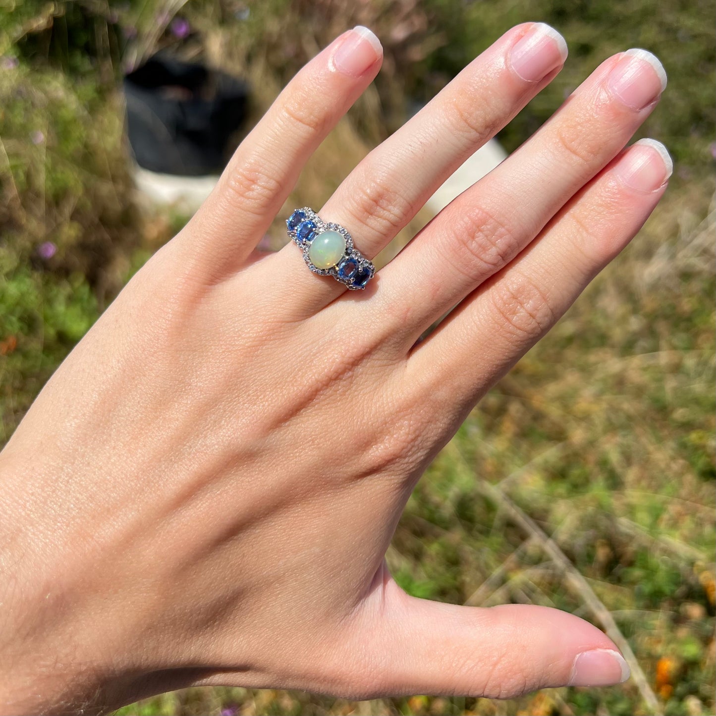 A sterling silver Ethiopian opal and kyanite ring worn on a hand in the sunlight.