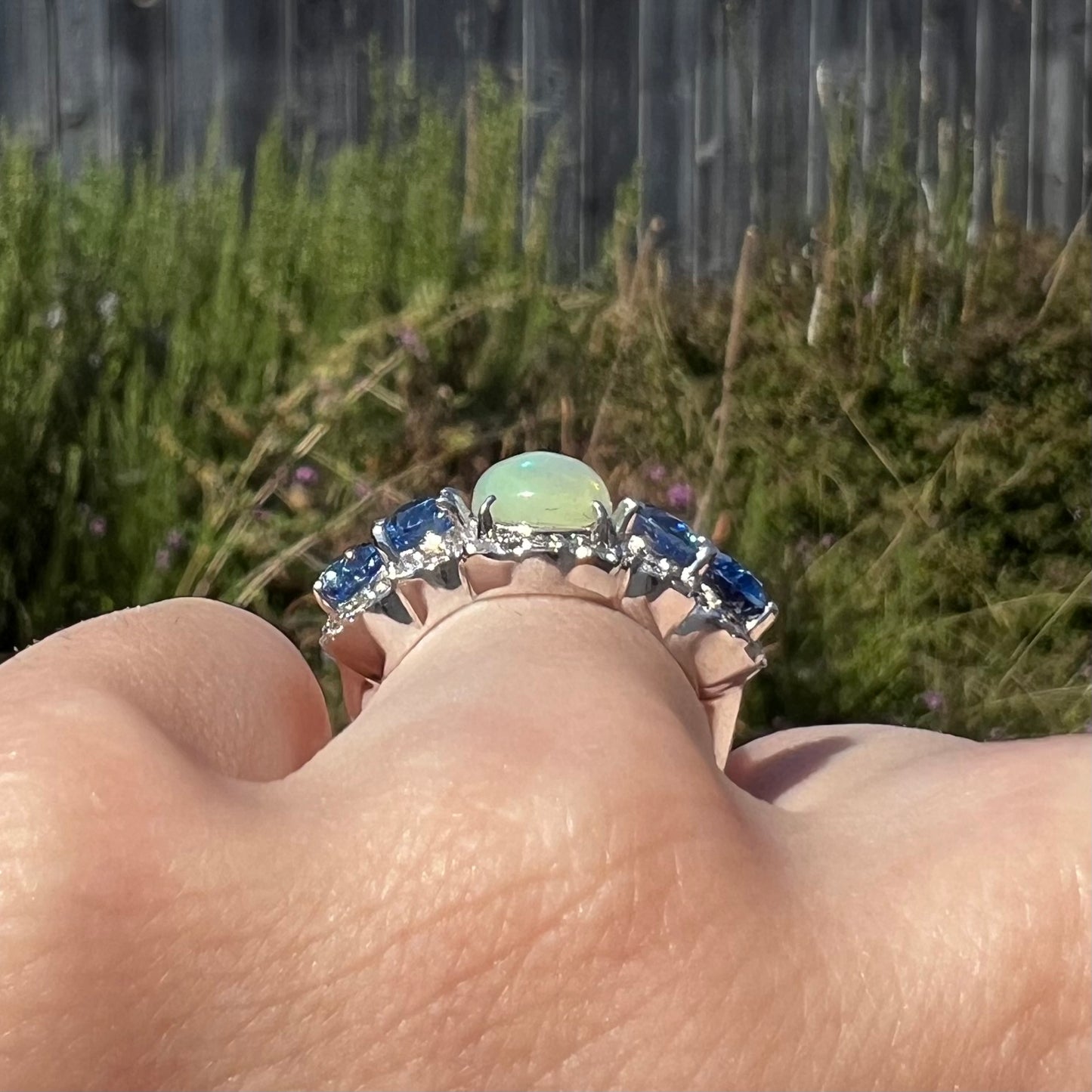 Close-up side gallery view of sterling silver Ethiopian opal and kyanite ring worn on a hand in the sunlight.