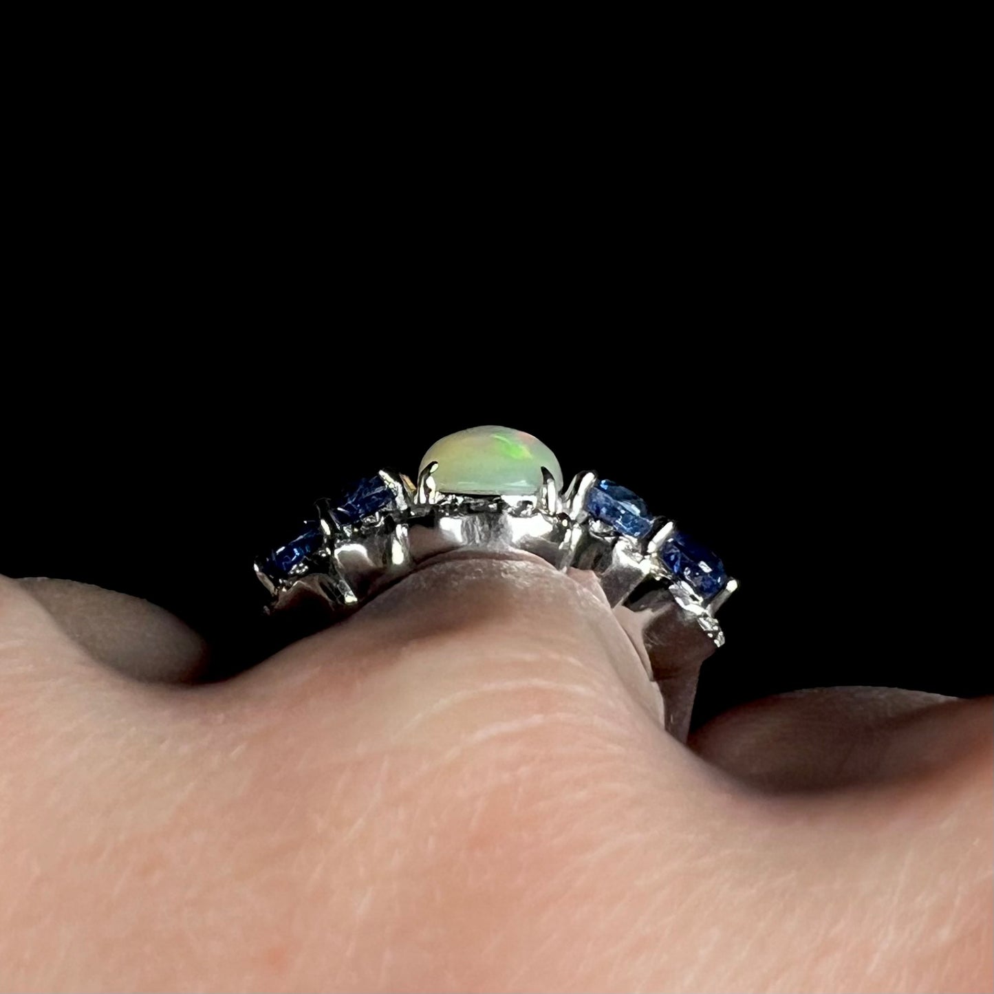 Close-up side gallery view of a sterling silver Ethiopian opal and kyanite ring worn on a hand.