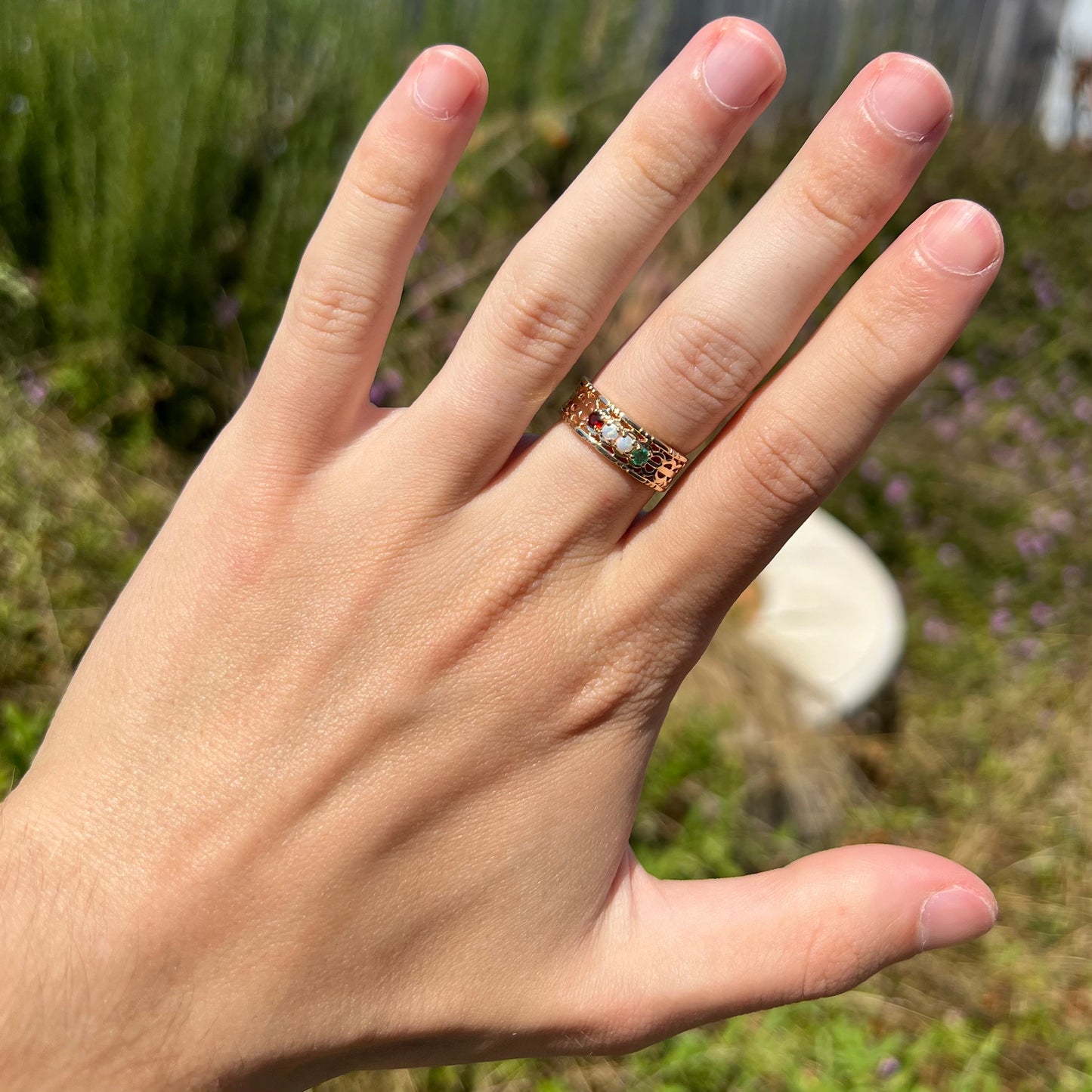 A gold woven-style mother's ring set with two opals, an emerald, and a garnet worn on a hand in sunlight.