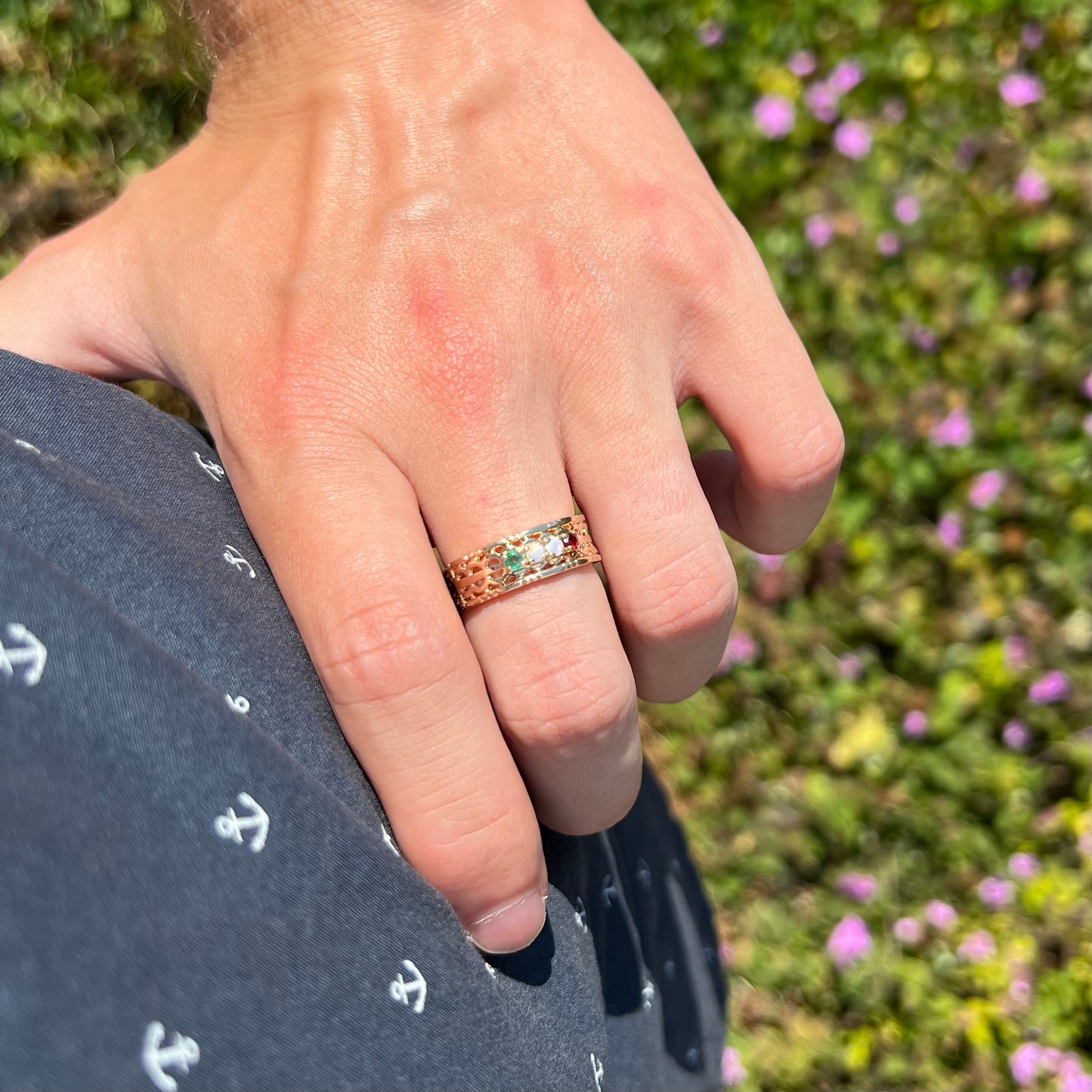 An opal, emerald, and garnet mother's ring worn on a hand in the sunlight as the hand rests on the model's hip.