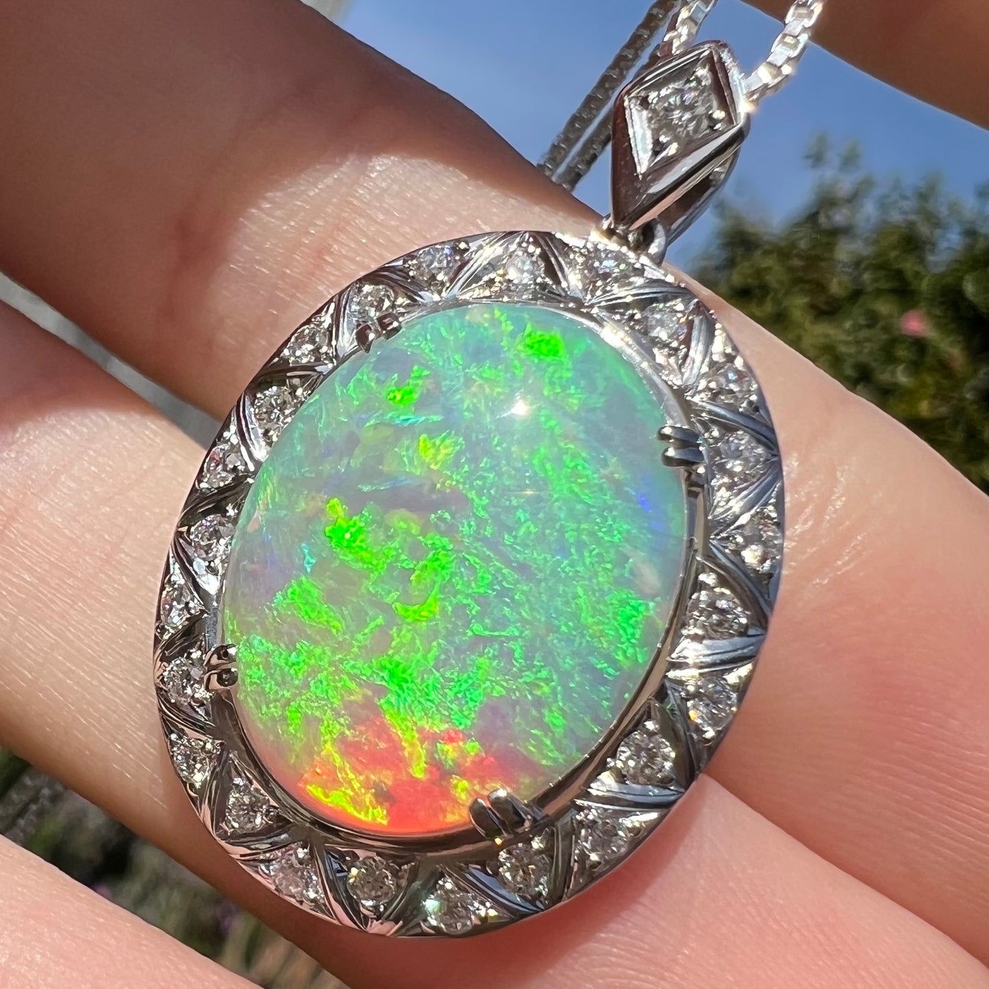 Slight angle of same opal pendant in sunlight, revealing a red flash within the green fire.