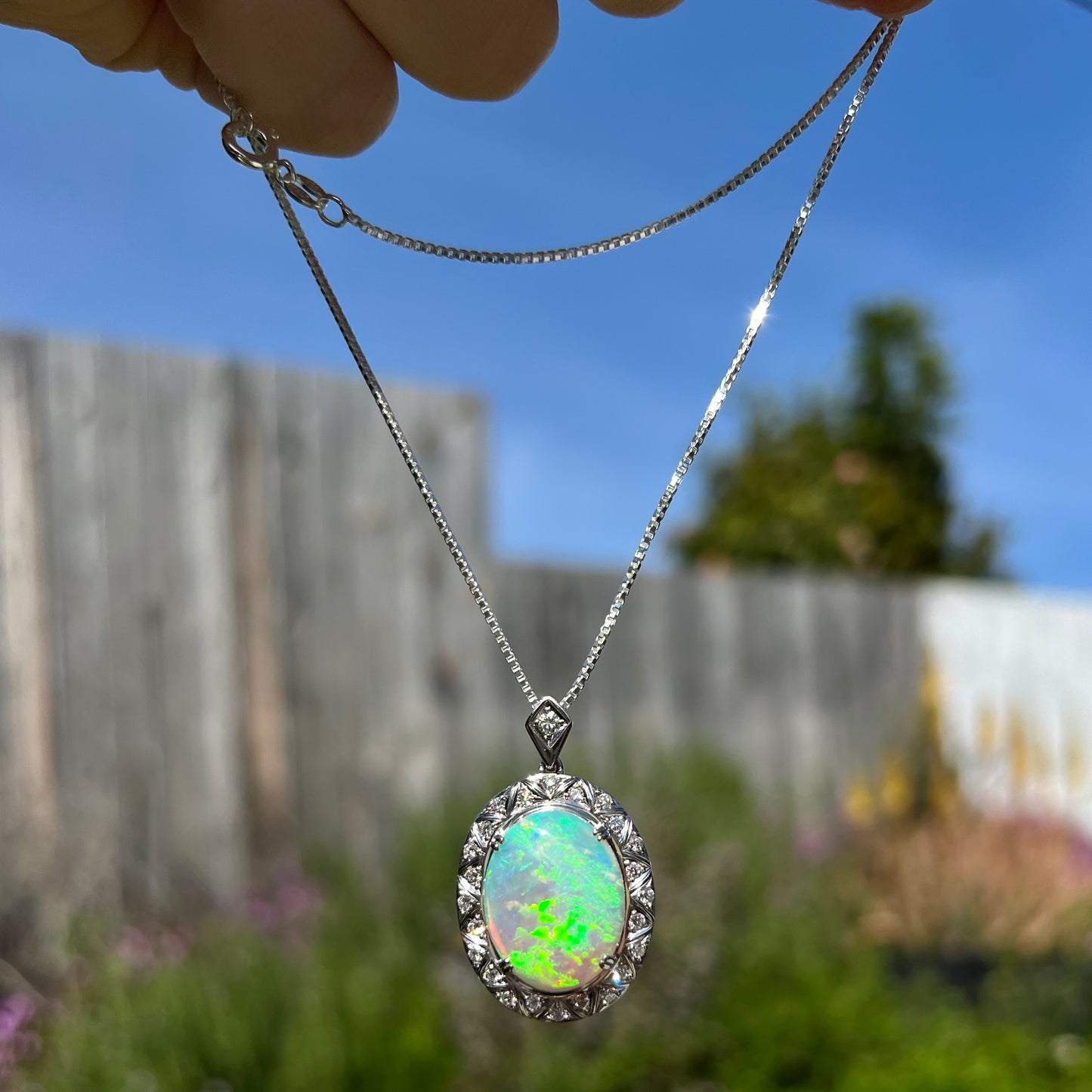 Outdoor photo of platinum opal necklace in sunlight, green fire visible.
