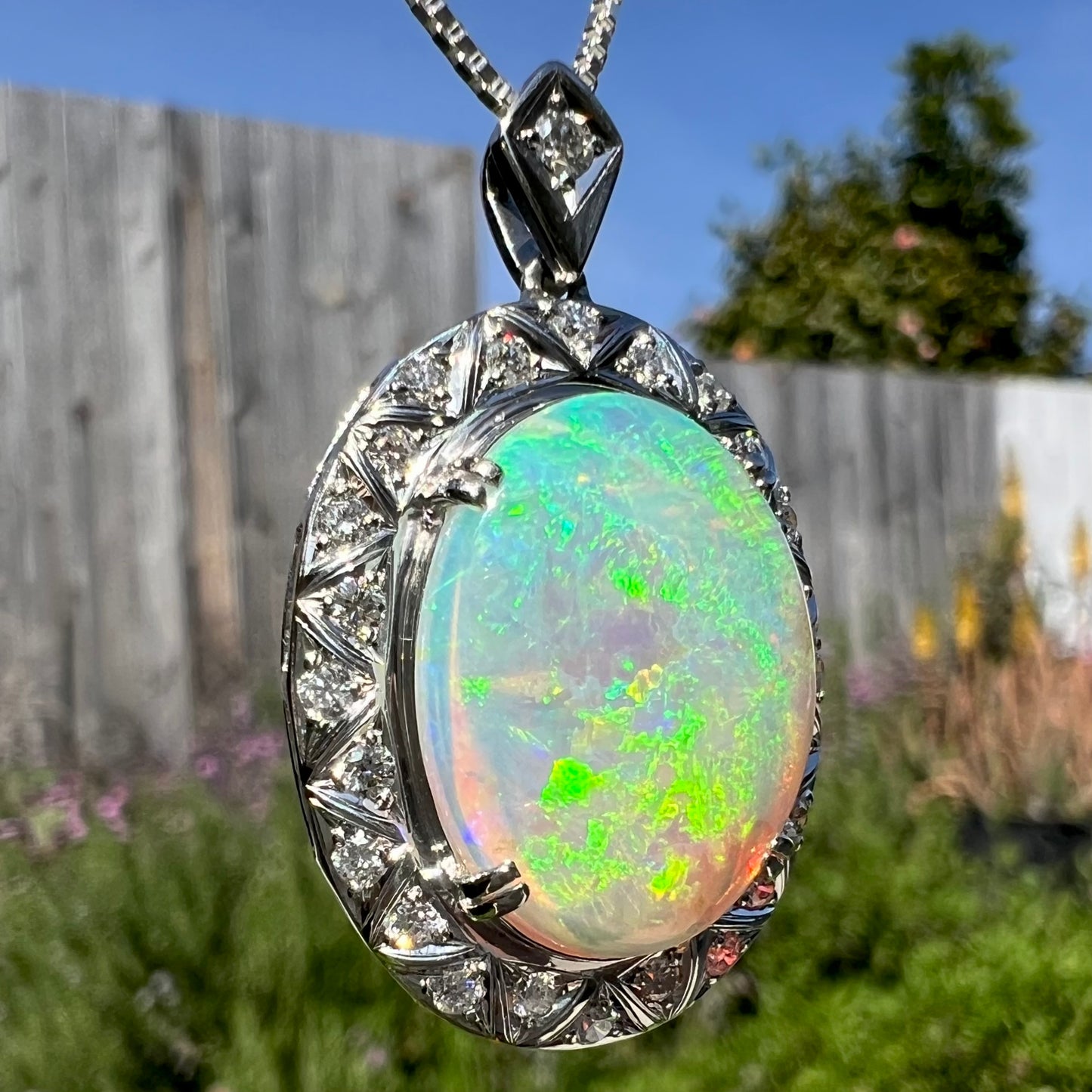 Close-up of opal pendant at an angle in sunlight, showing green and yellow hues.