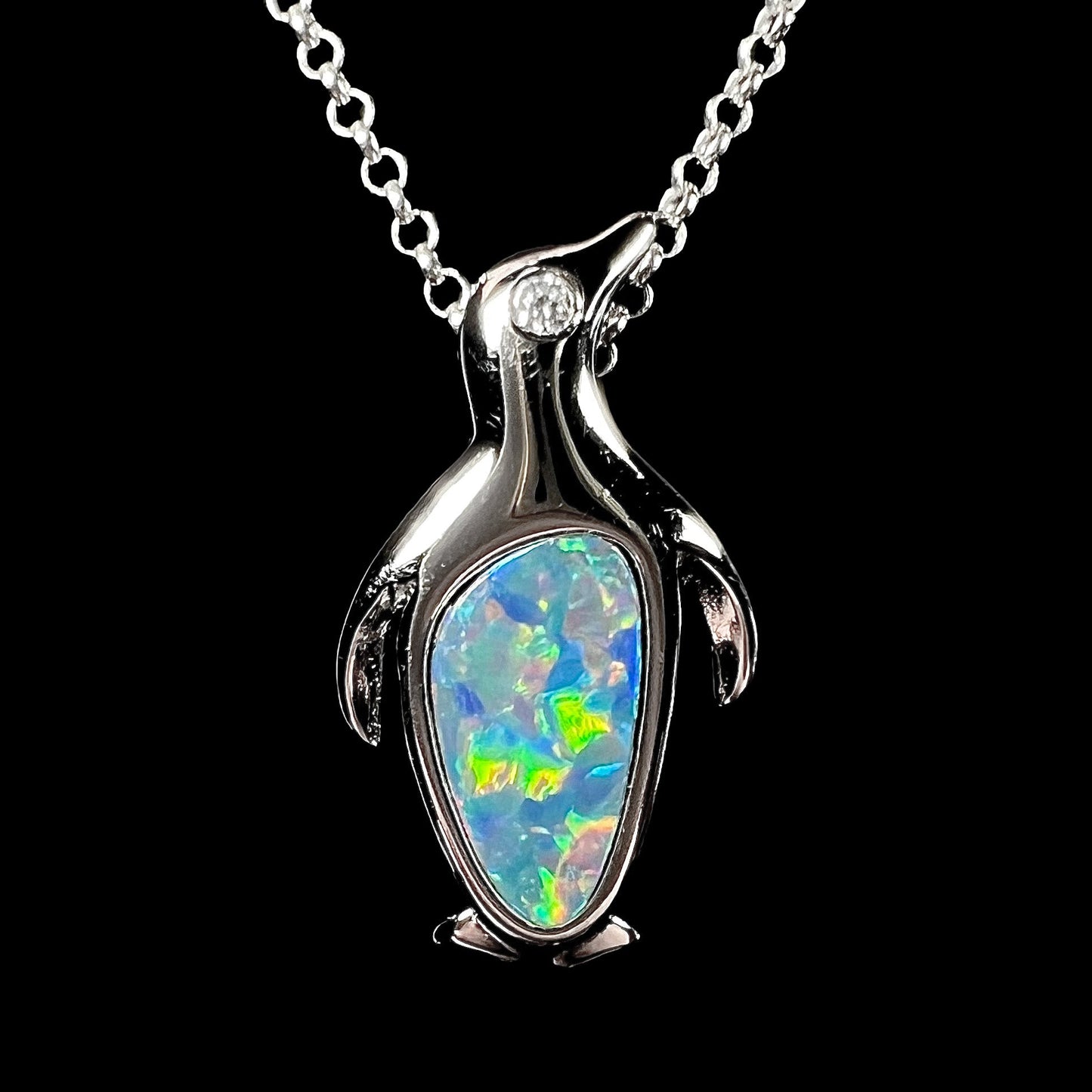 A sterling silver penguin necklace inlaid with a black opal doublet and a CZ accent in the penguin's eye.
