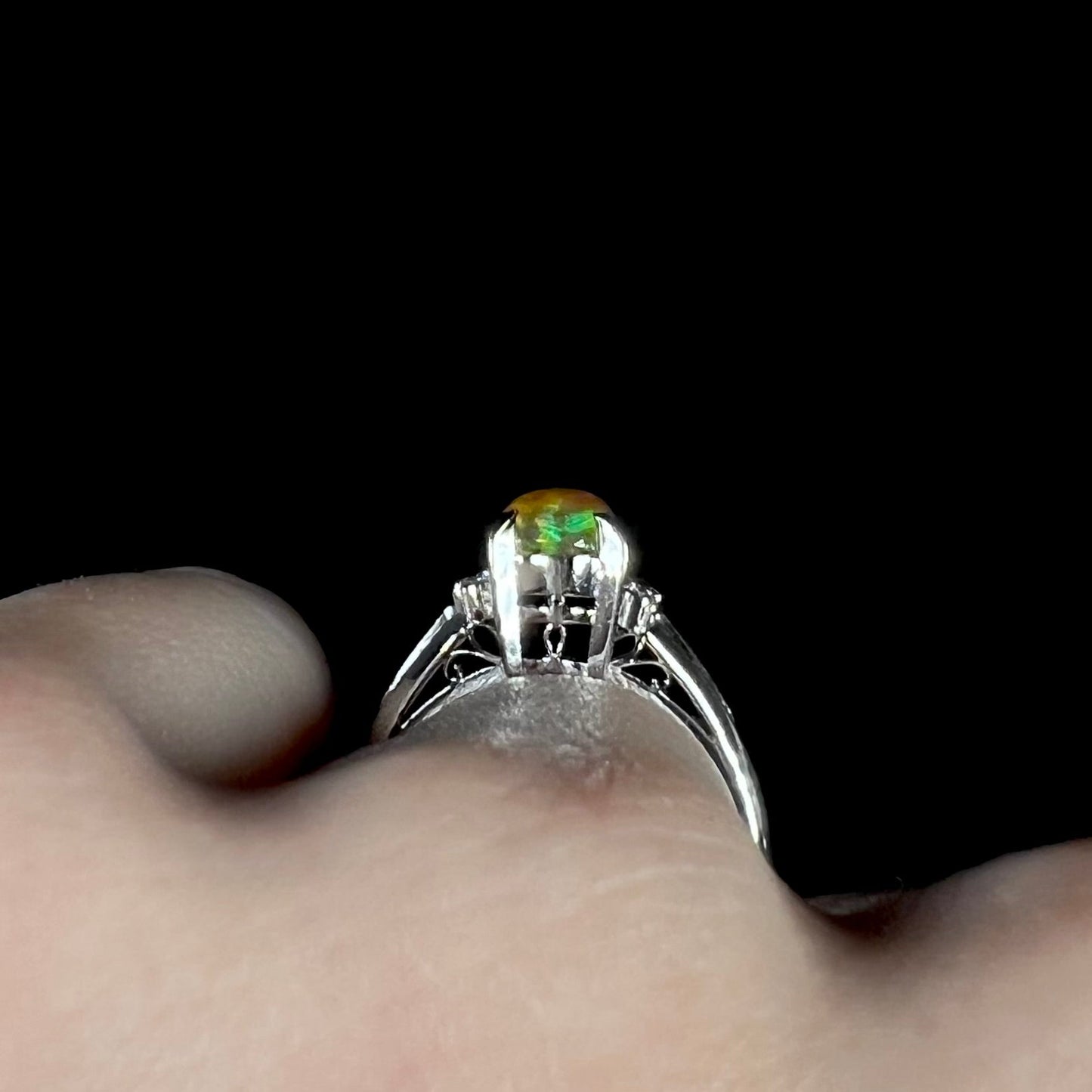 A platinum filigree and diamond-accented Mexican fire opal ring. The opal is orange with green fire.