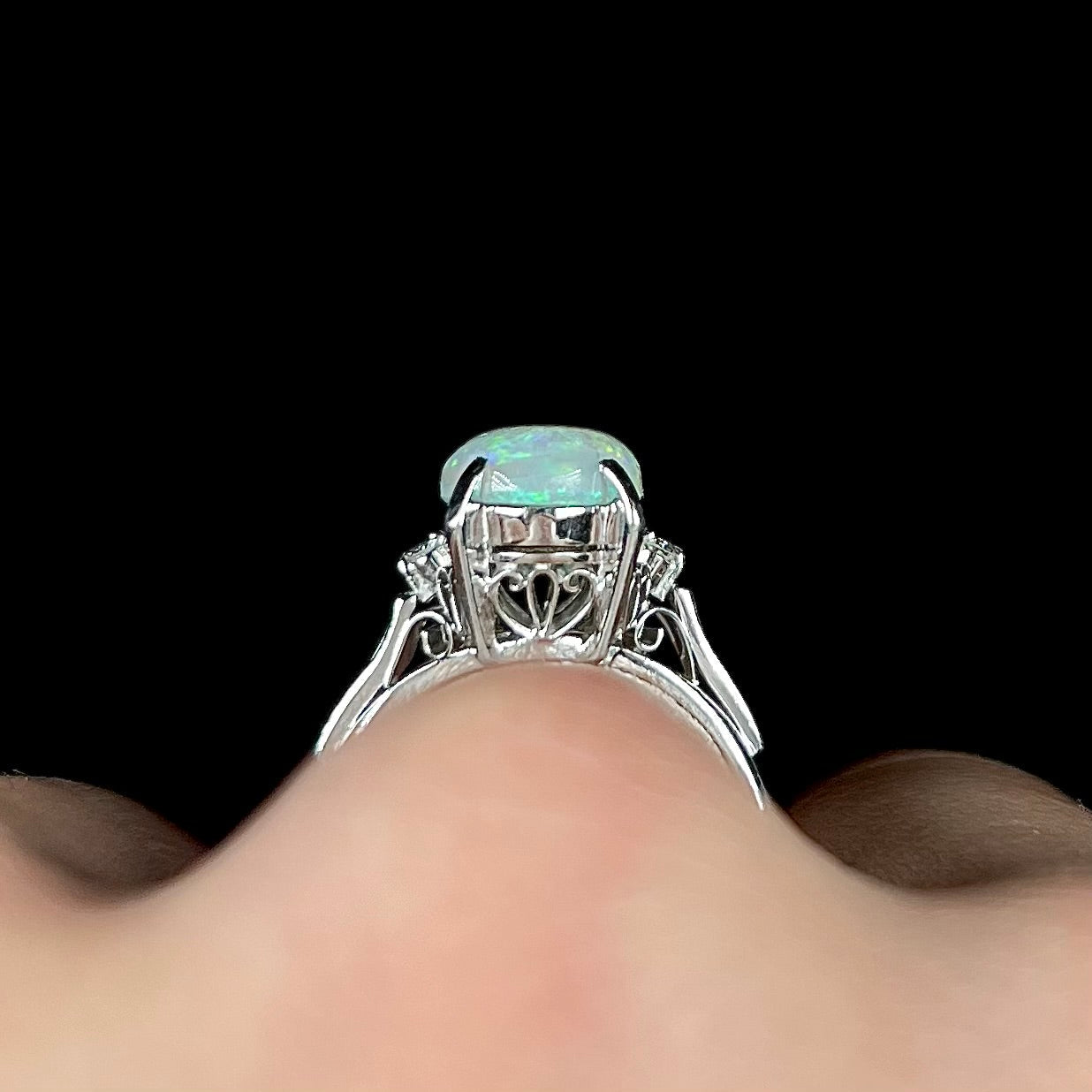 A platinum filigree opal engagement ring set with diamond accents. The opal has green-blue colors.