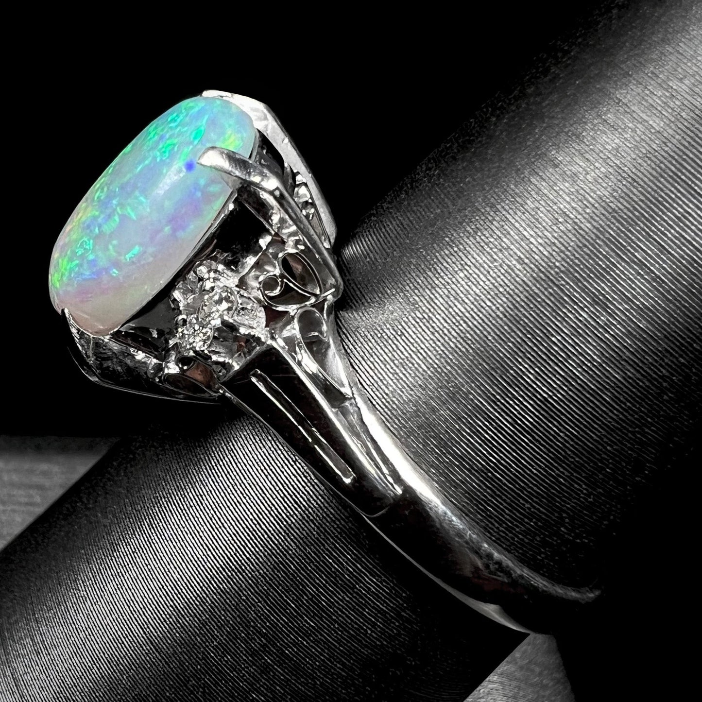 A platinum filigree opal engagement ring set with diamond accents. The opal has green-blue colors.