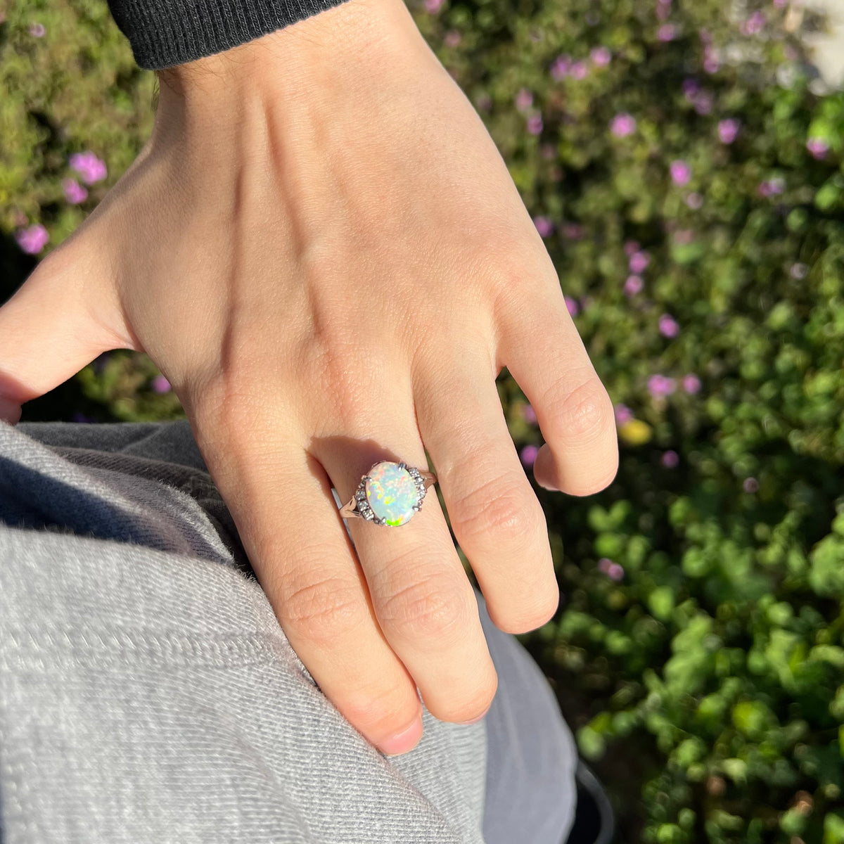Oval shaped 2.35ct Australian opal ring worn on hand as it rests on person's hip in sunlight; six diamond accents seen at top of platinum shank
