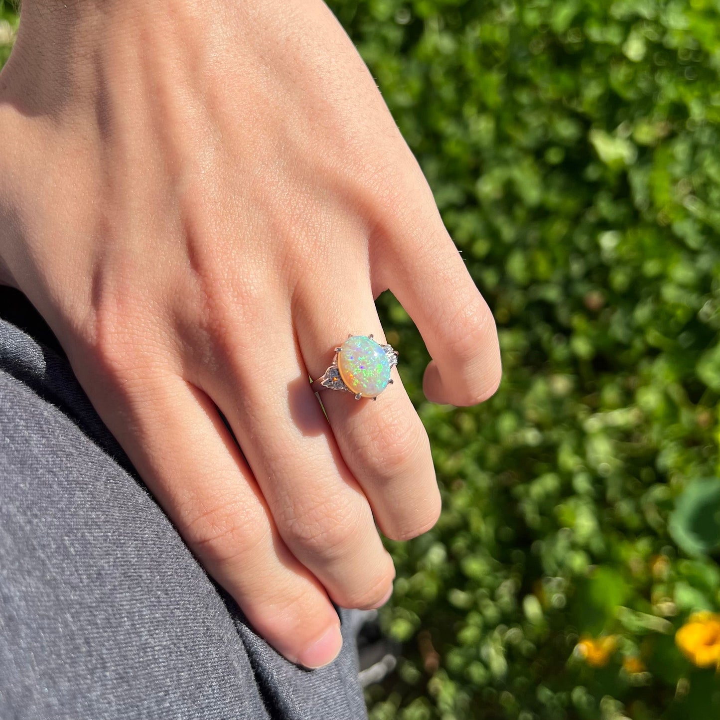 An Australian crystal opal and diamond engagement ring set in a platinum filigree mounting. The opal plays green/blue colors and has a crack.