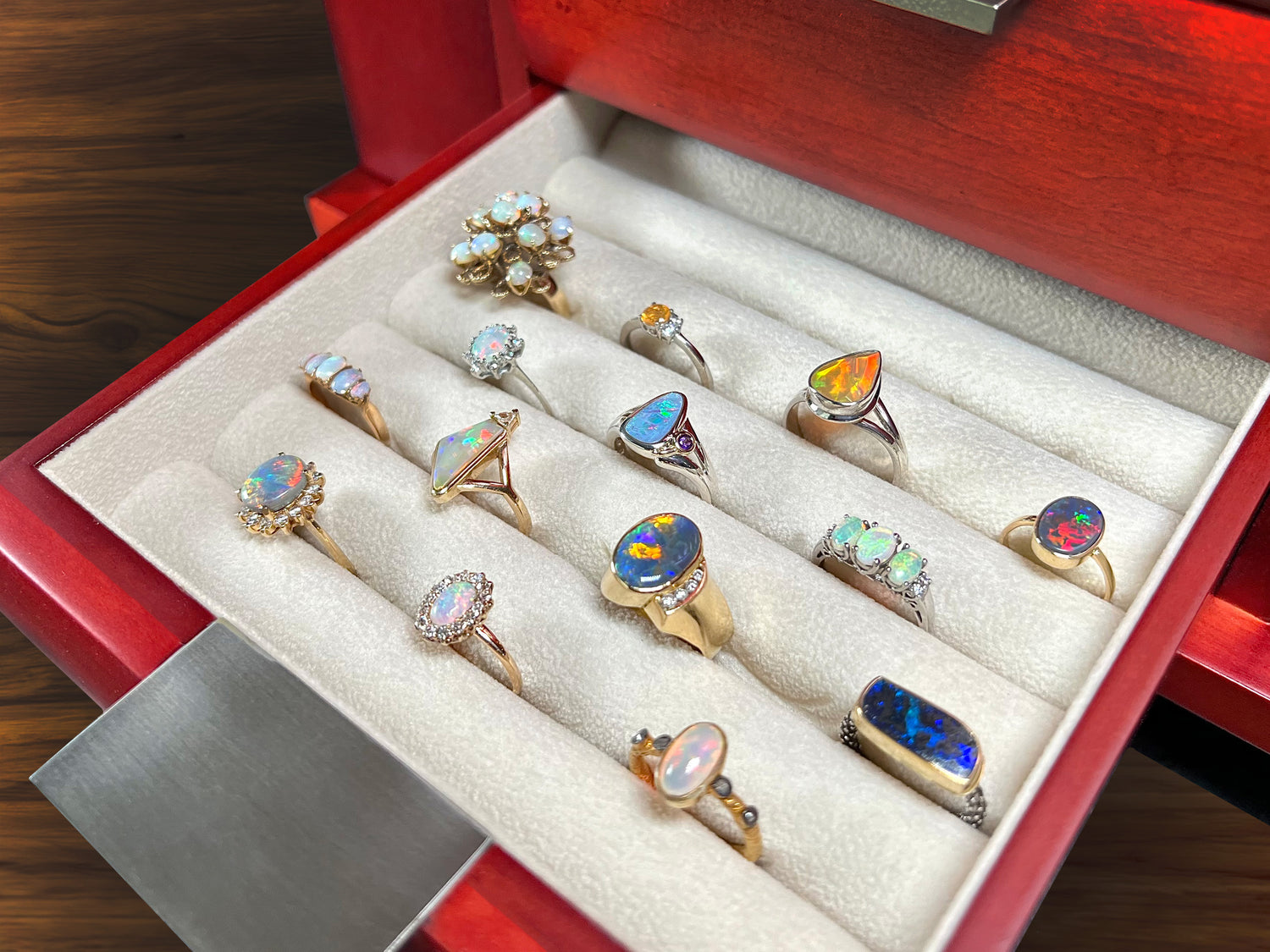 Fourteen natural opal rings shown resting in the open drawer of a cherrywood jewelry box.