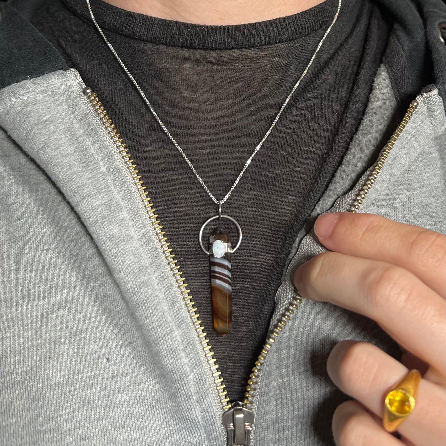 An opal and sardonyx crystal necklace, worn around a model's neck with a dark shirt and partially unzipped hoodie.
