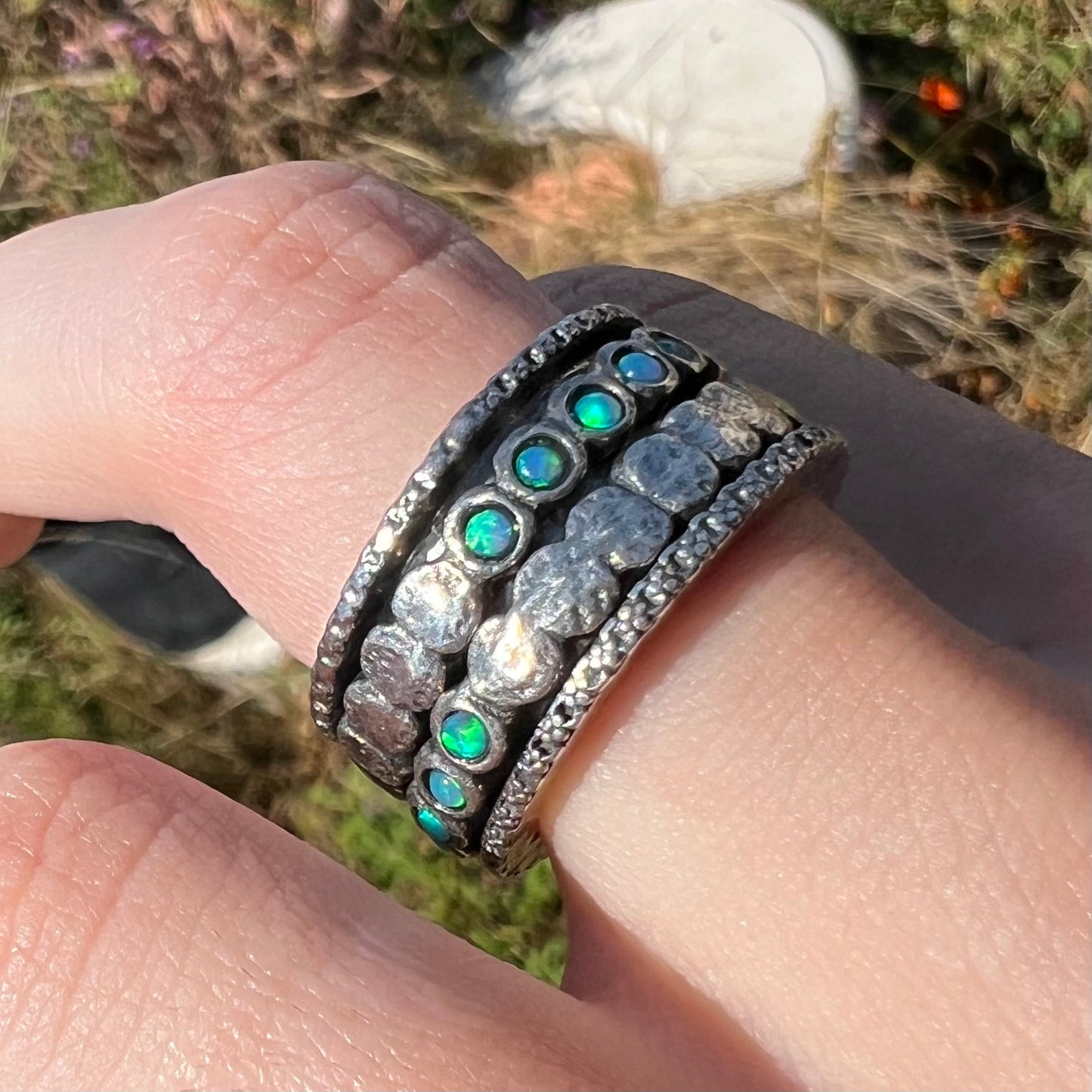 An opal spinner ring worn on a finger in sunlight. The opals are round and show faint green color play.