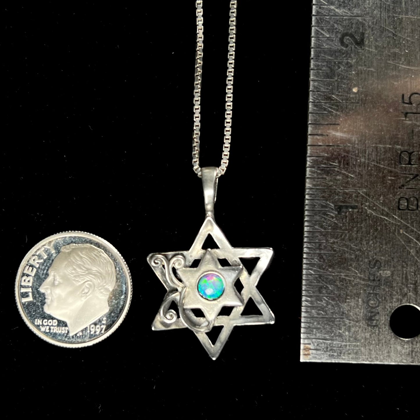 An opal Star of David necklace shown next to a dime coin and ruler for scale.